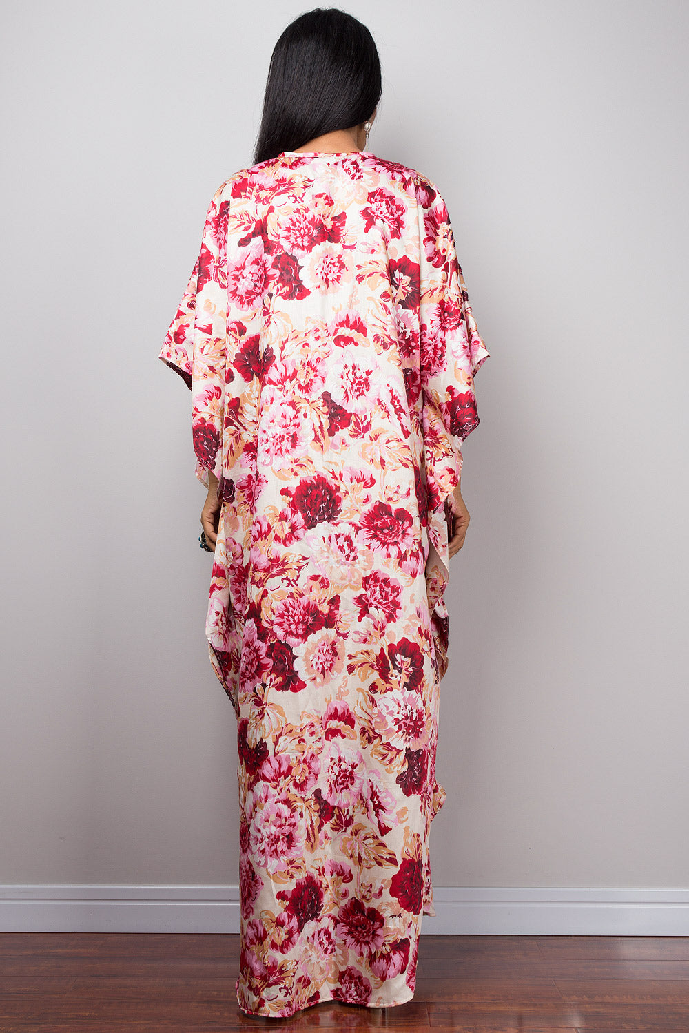 Petite woman wearing a pink floral dress standing against a plain wall.