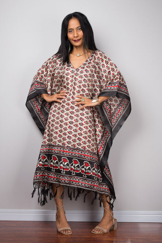 Woman wearing a patterned caftan dress with fringe against a plain background
