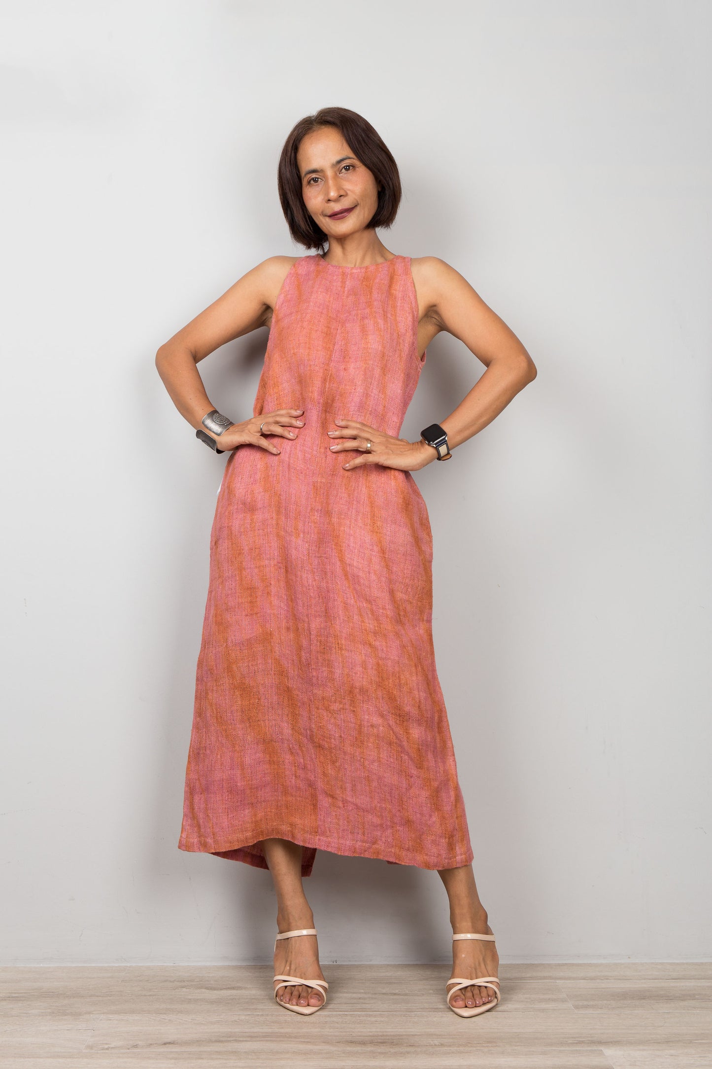 Woman wearing a sleeveless pink coral dress standing against a plain background.  Organic hemp dress with shibori tie dye details.