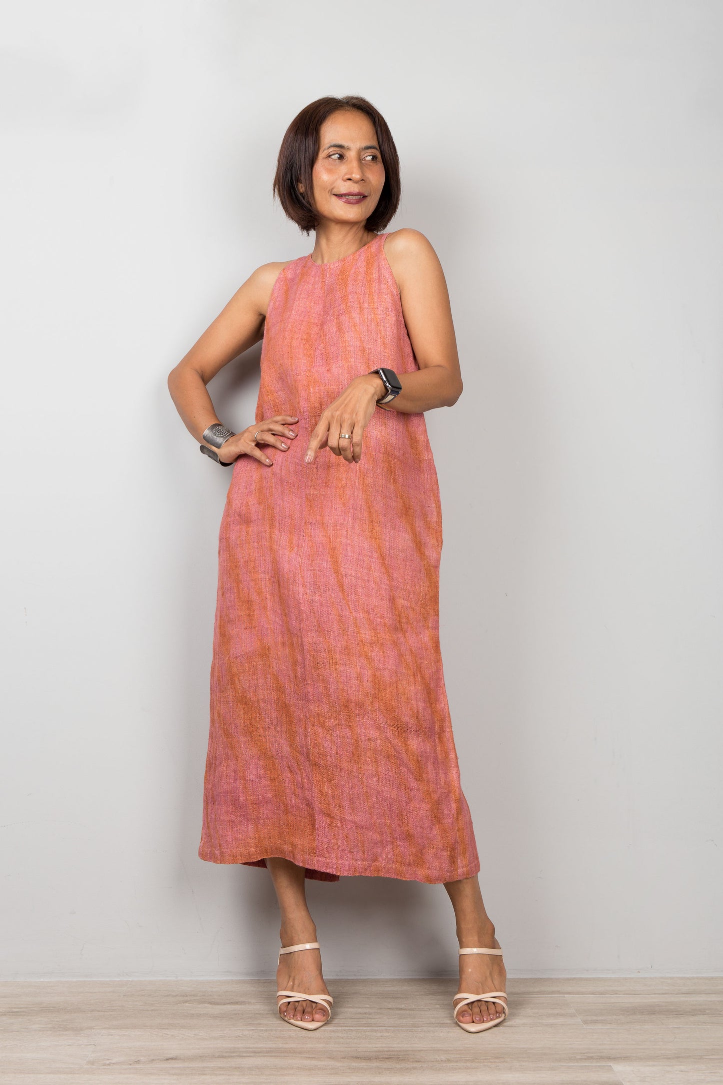Woman wearing a sleeveless pink coral dress for petite, standing against a plain background.  Handwoven organic hemp dress with shibori tie dye details.
