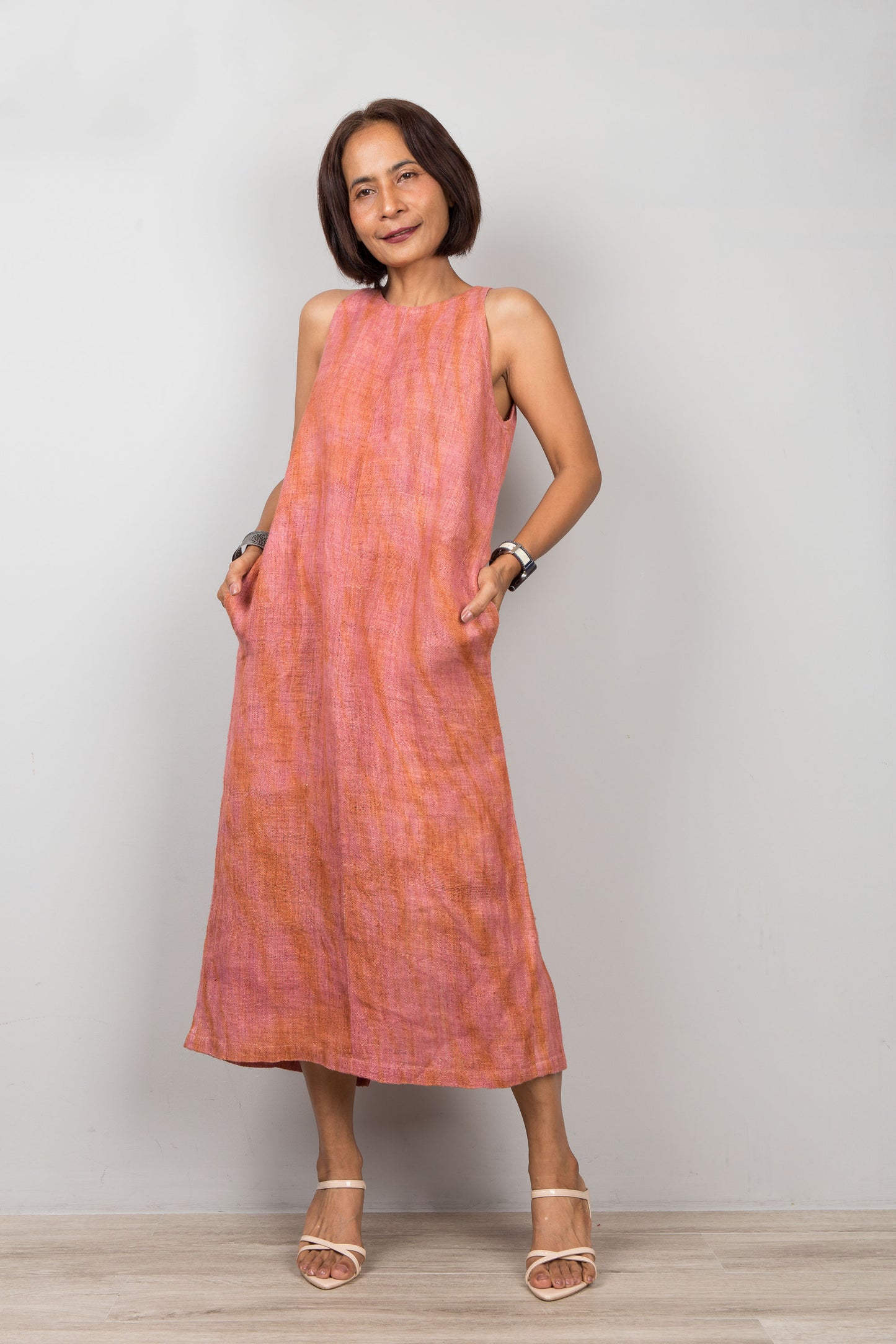 Woman wearing a coral dress standing against a plain background.  Sleeveless hemp dress with shibori tie dye details.