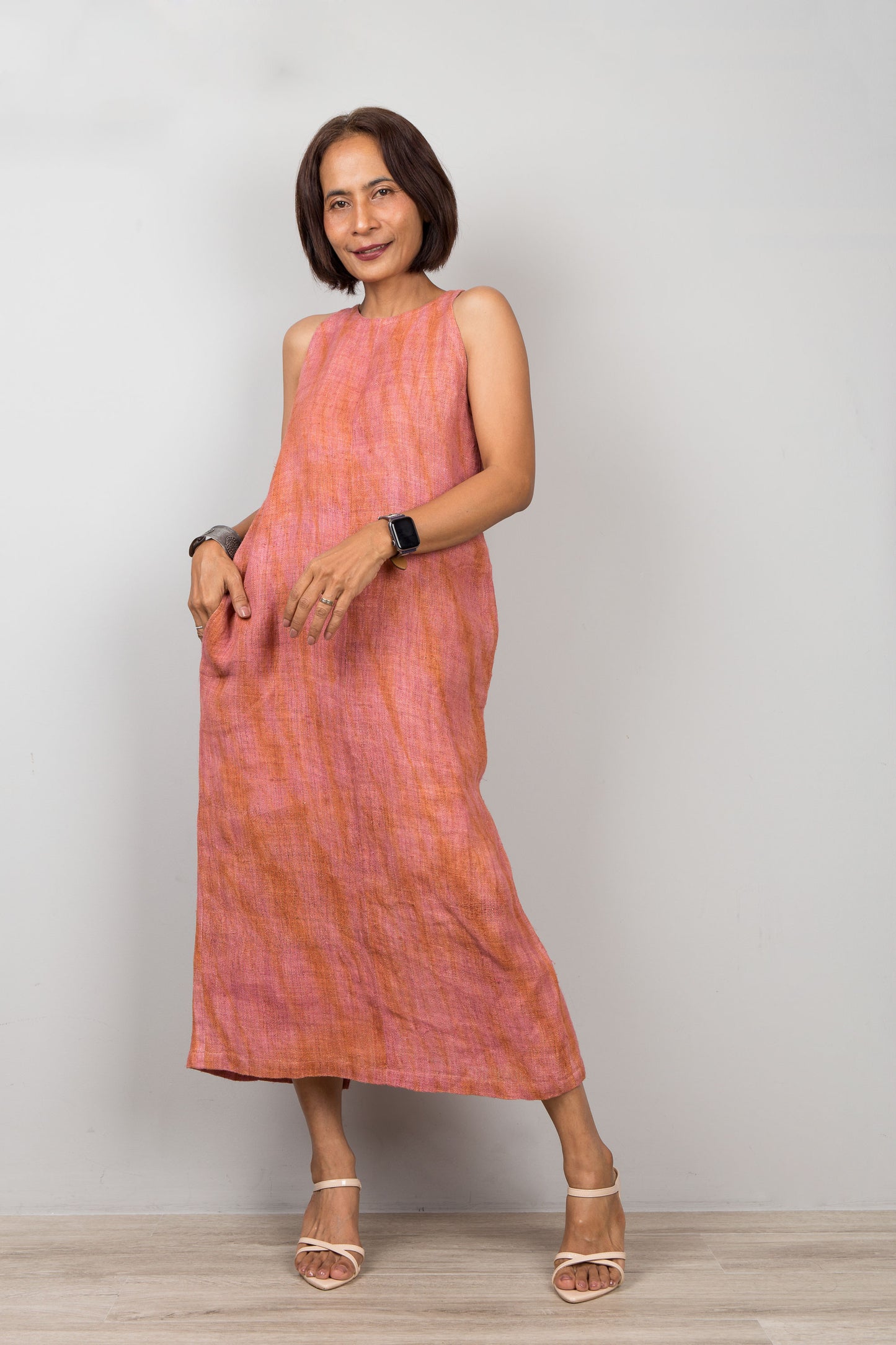 Woman wearing a pink coral dress for petite standing against a plain background.  Sleeveless hemp dress with shibori tie dye details.