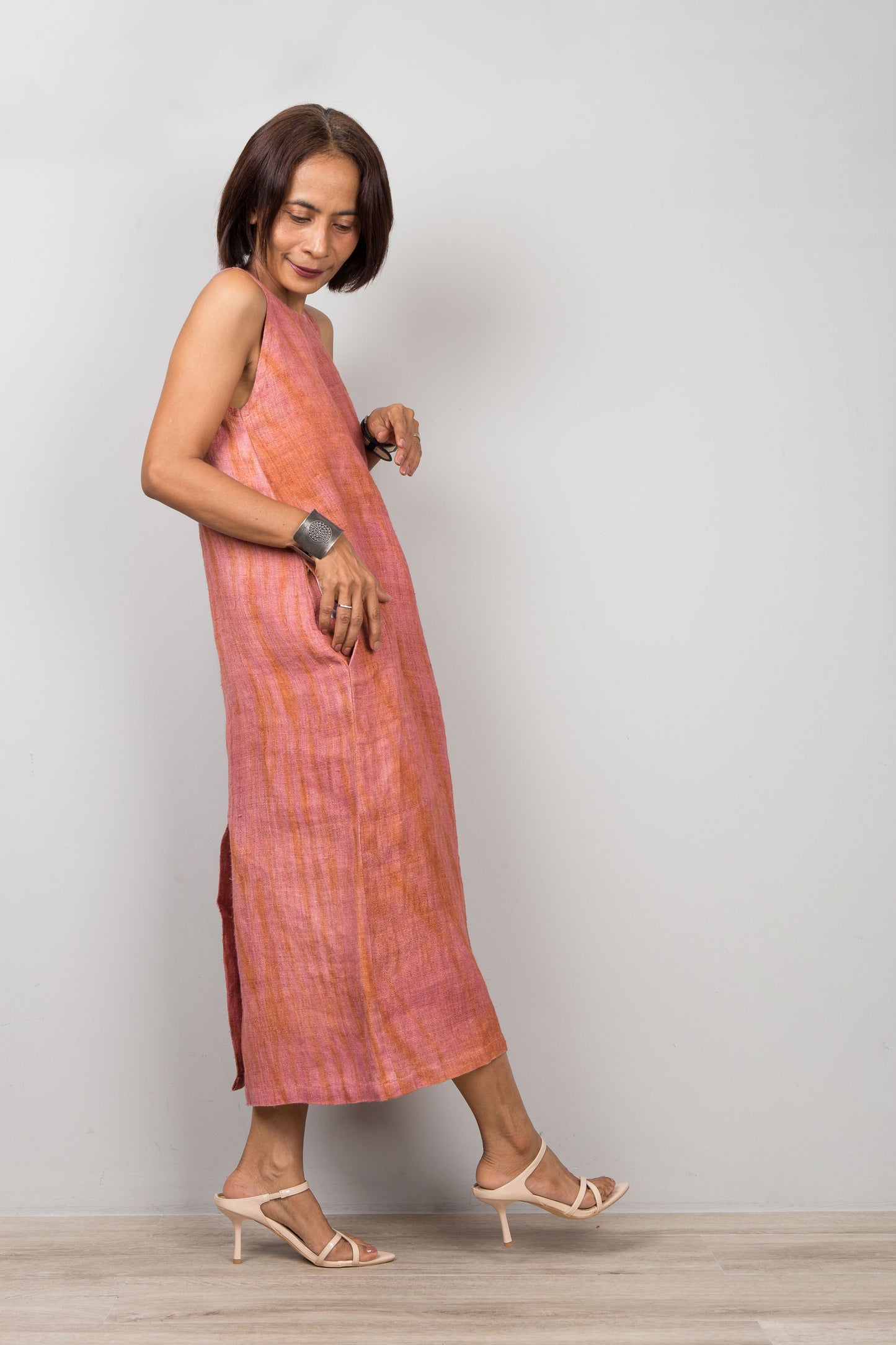 Woman wearing a sleeveless pink coral dress for petite standing against a plain background.  Handwoven hemp dress with shibori tie dye details.