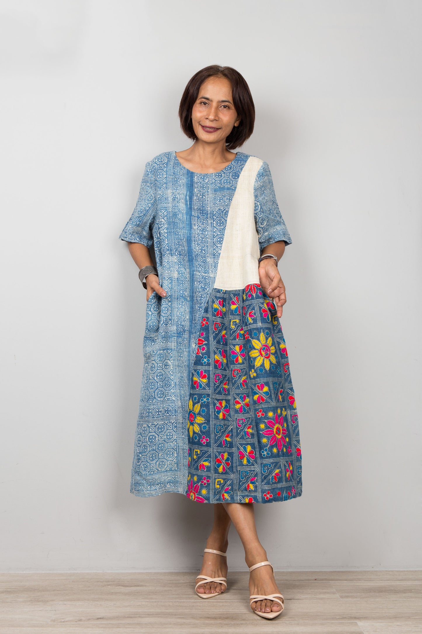 Nuichan wearing a blue batik hemp kaftan with floral embroidery against a plain background