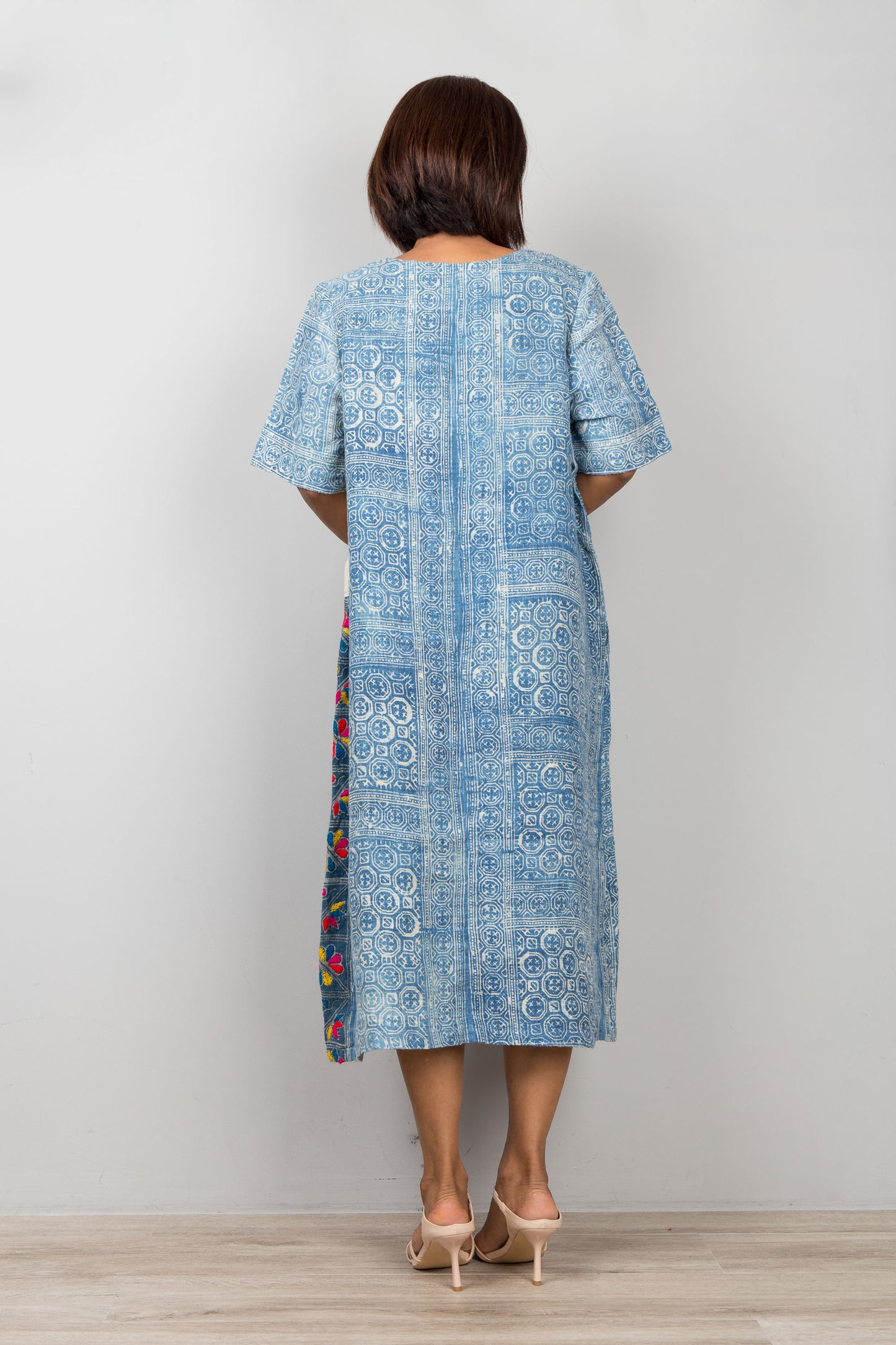 Nuichan wearing a blue batik caftan dress, for petite, with floral embroidery against a plain background
