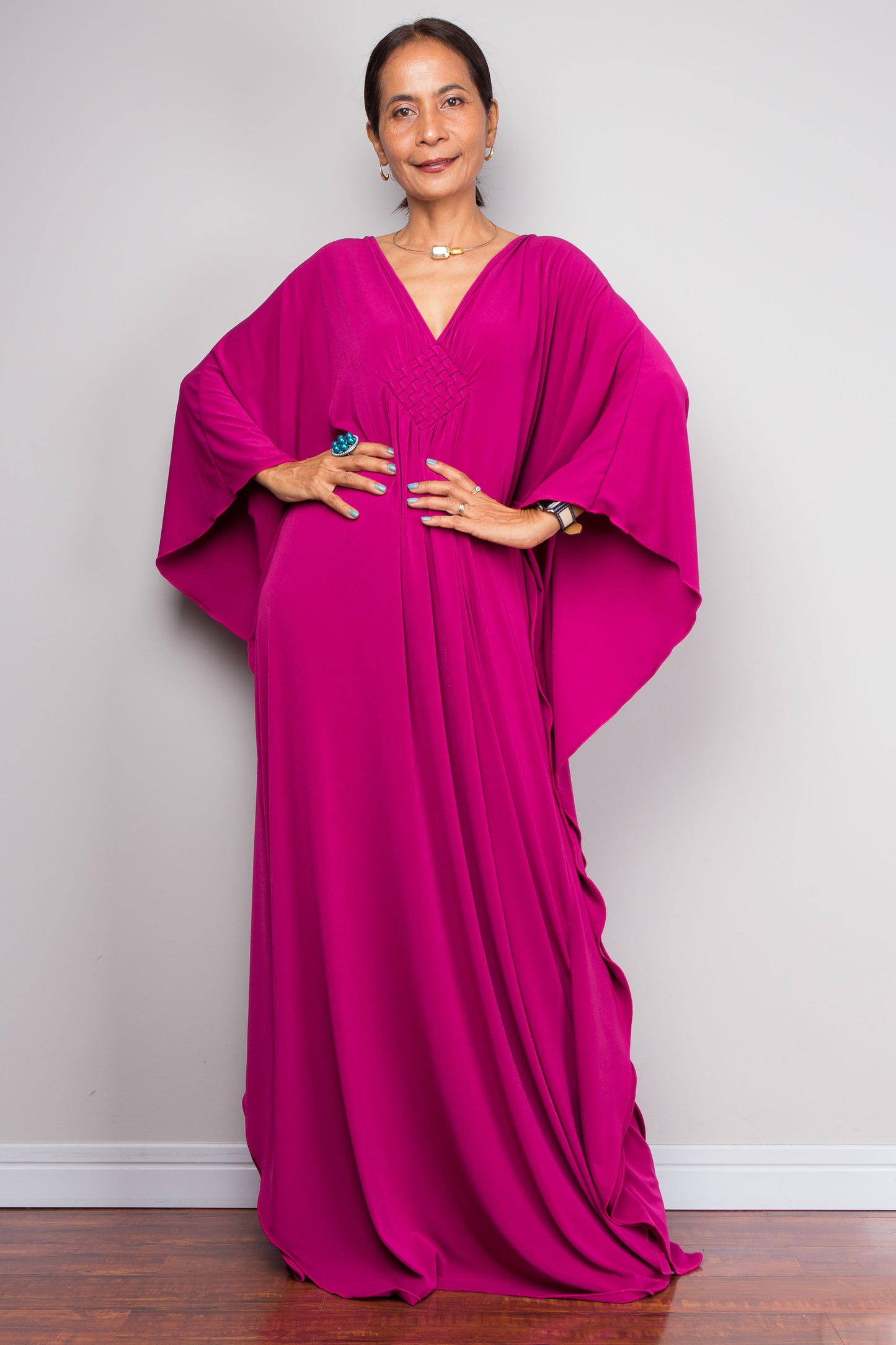 Woman wearing a vibrant pink kaftan dress against a plain background