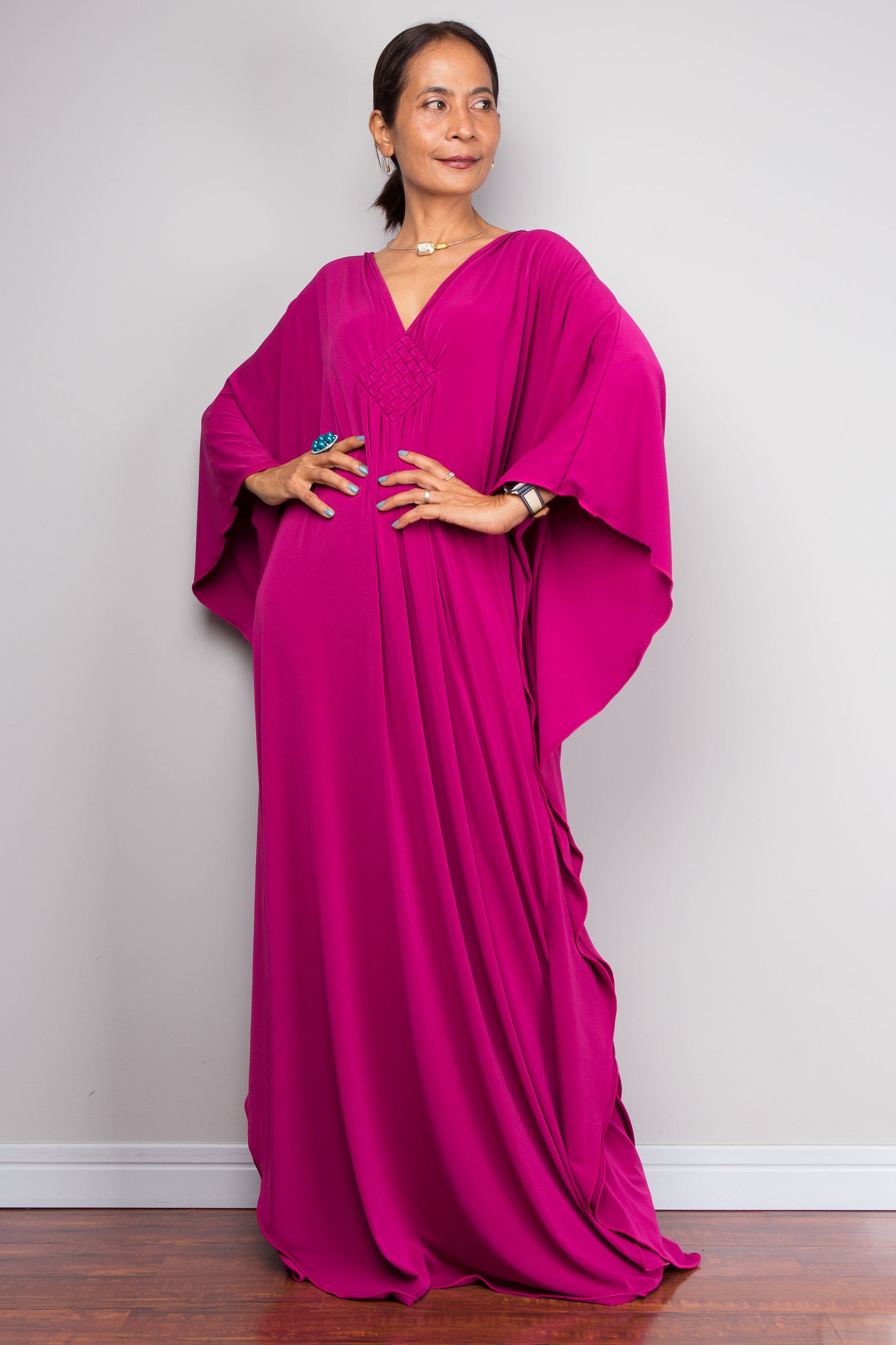 Woman wearing a vivid pink kaftan dress against a plain background