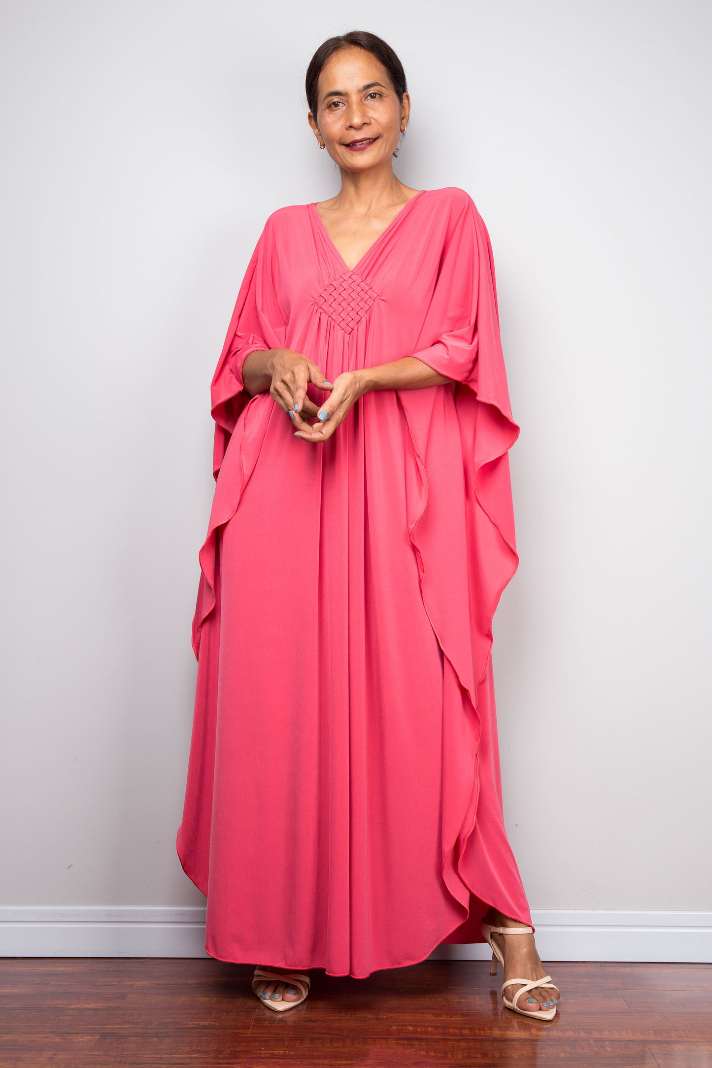 Front view of model in solid pink petite caftan dress with handmade braided diamond neckline detailing and fluid butterfly sleeves.