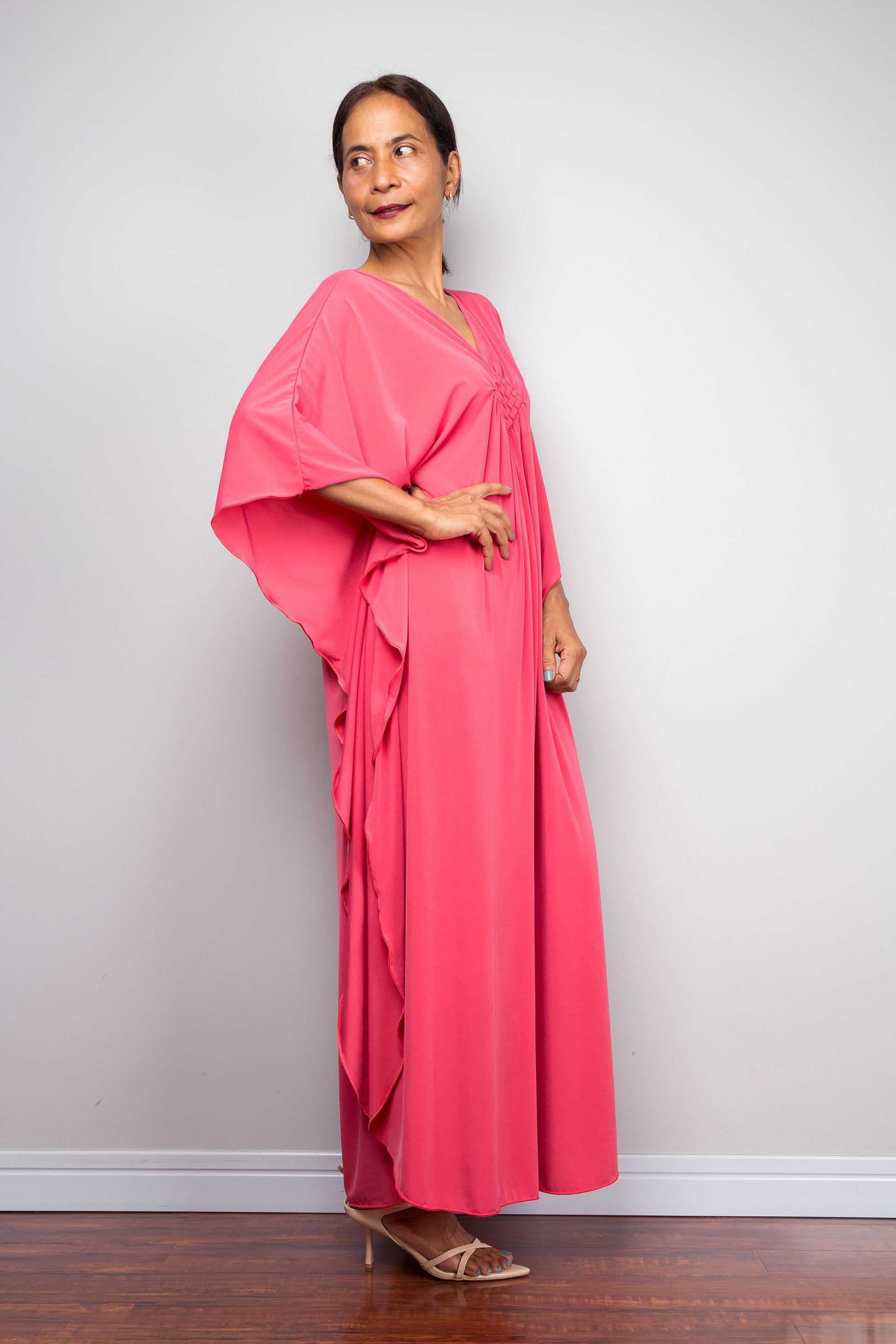 Side view of Woman wearing a pink caftan dress standing against a plain background