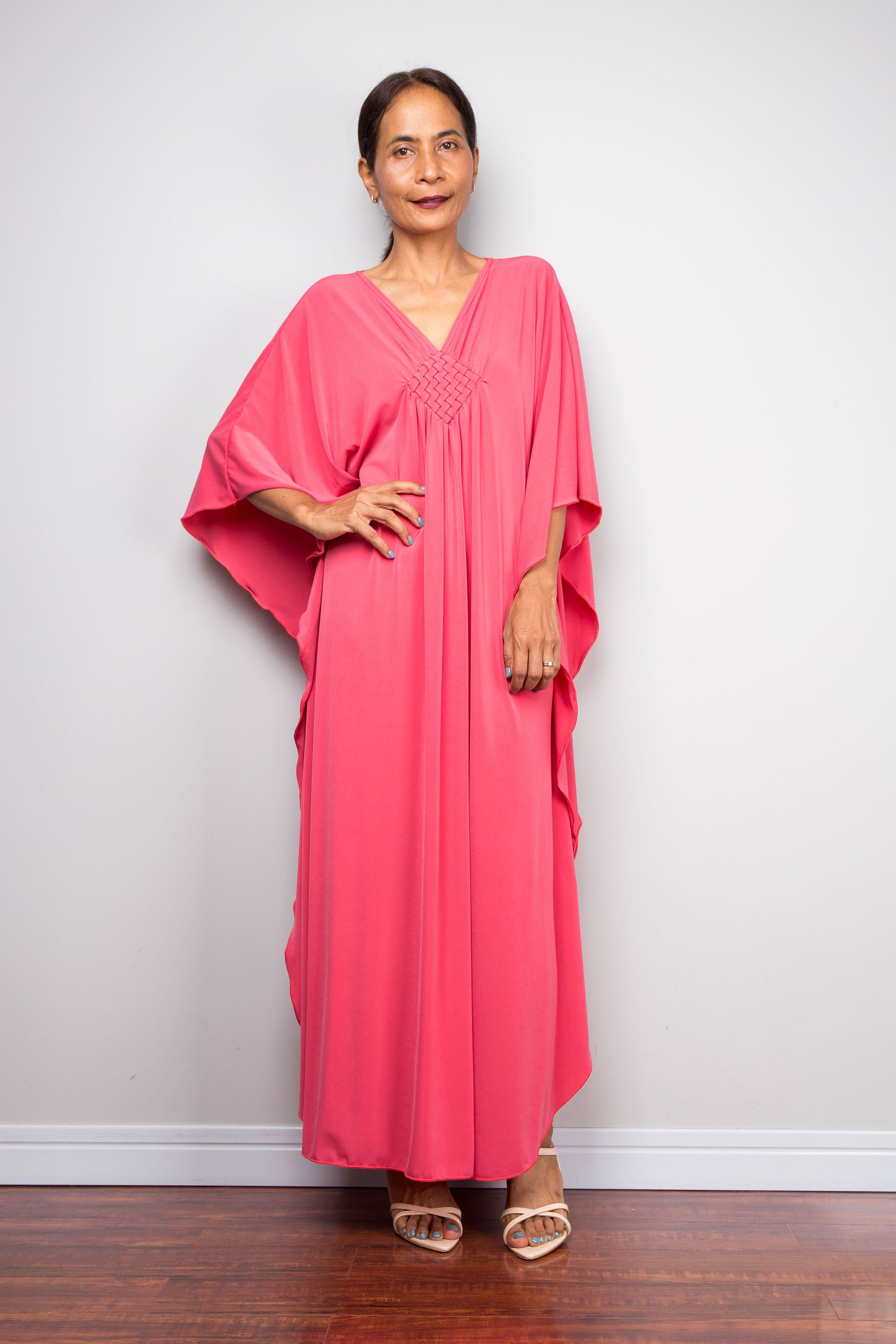 Woman wearing a pink dress standing against a plain white wall.