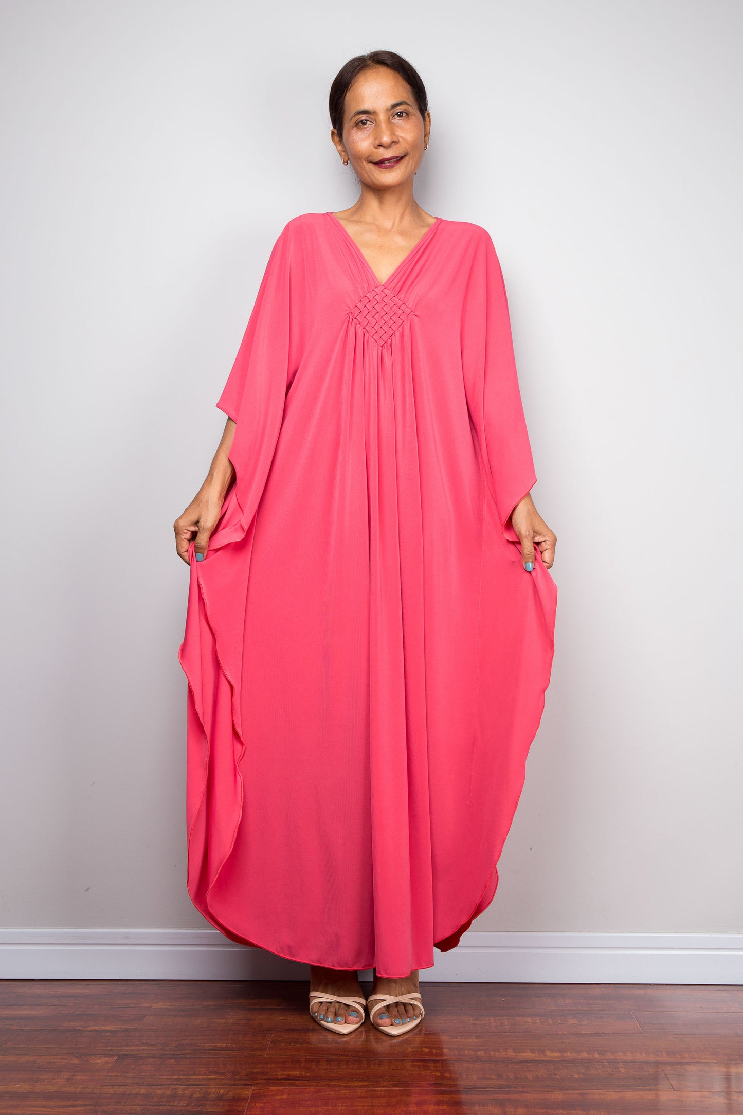 Petite Woman wearing a pink caftan dress against a white wall