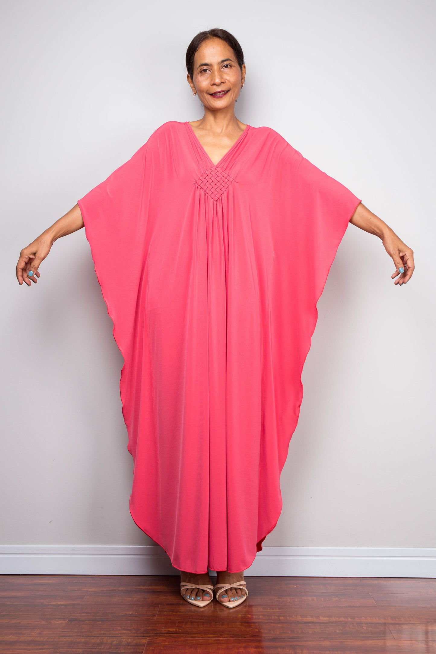 Front view of female model in solid pink petite caftan dress with handmade braided diamond neckline detailing and fluid butterfly sleeves.