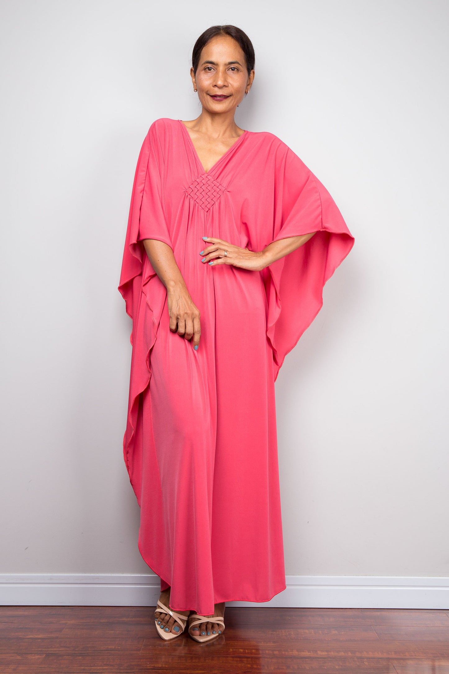 Woman wearing a pink petite caftan by Nuichan against a white wall