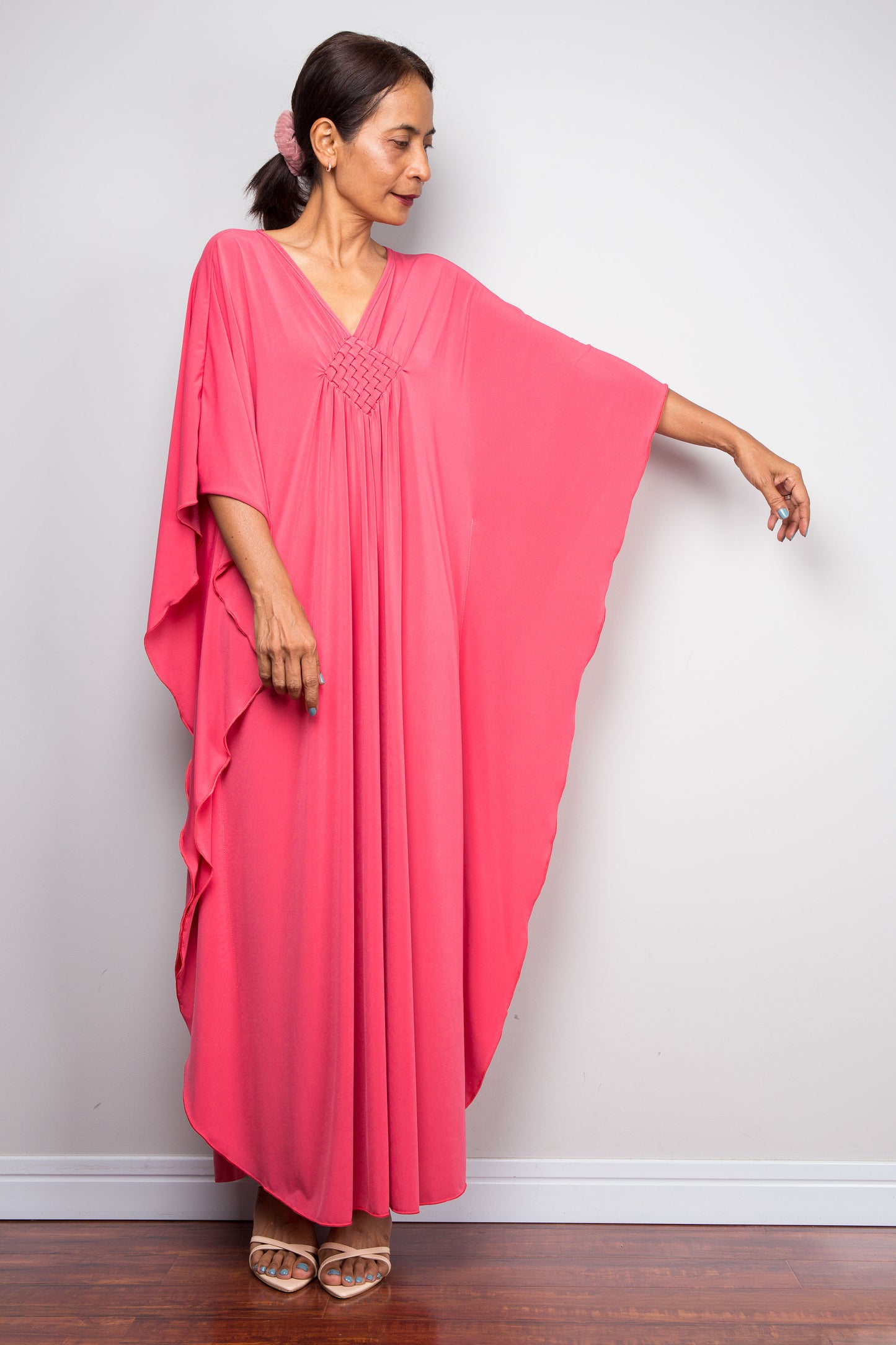 Front view of model in solid pink petite caftan dress with handmade braided diamond neckline detailing and a stretchd out butterfly sleeve