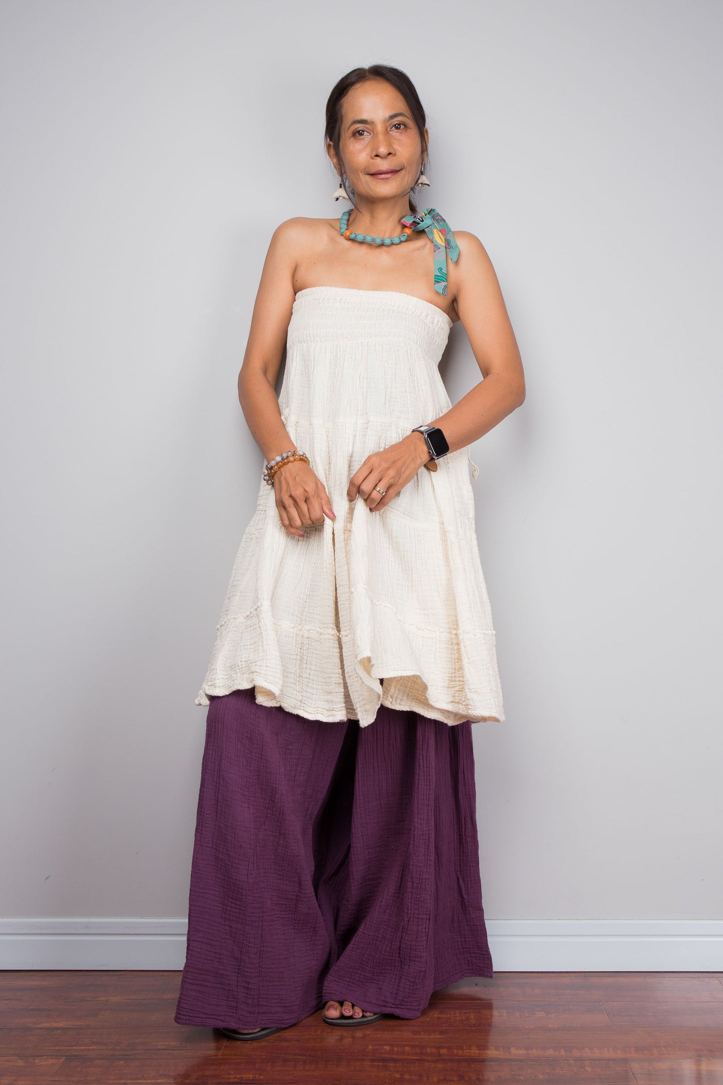 Woman wearing a white top and purple cotton pants against a plain background