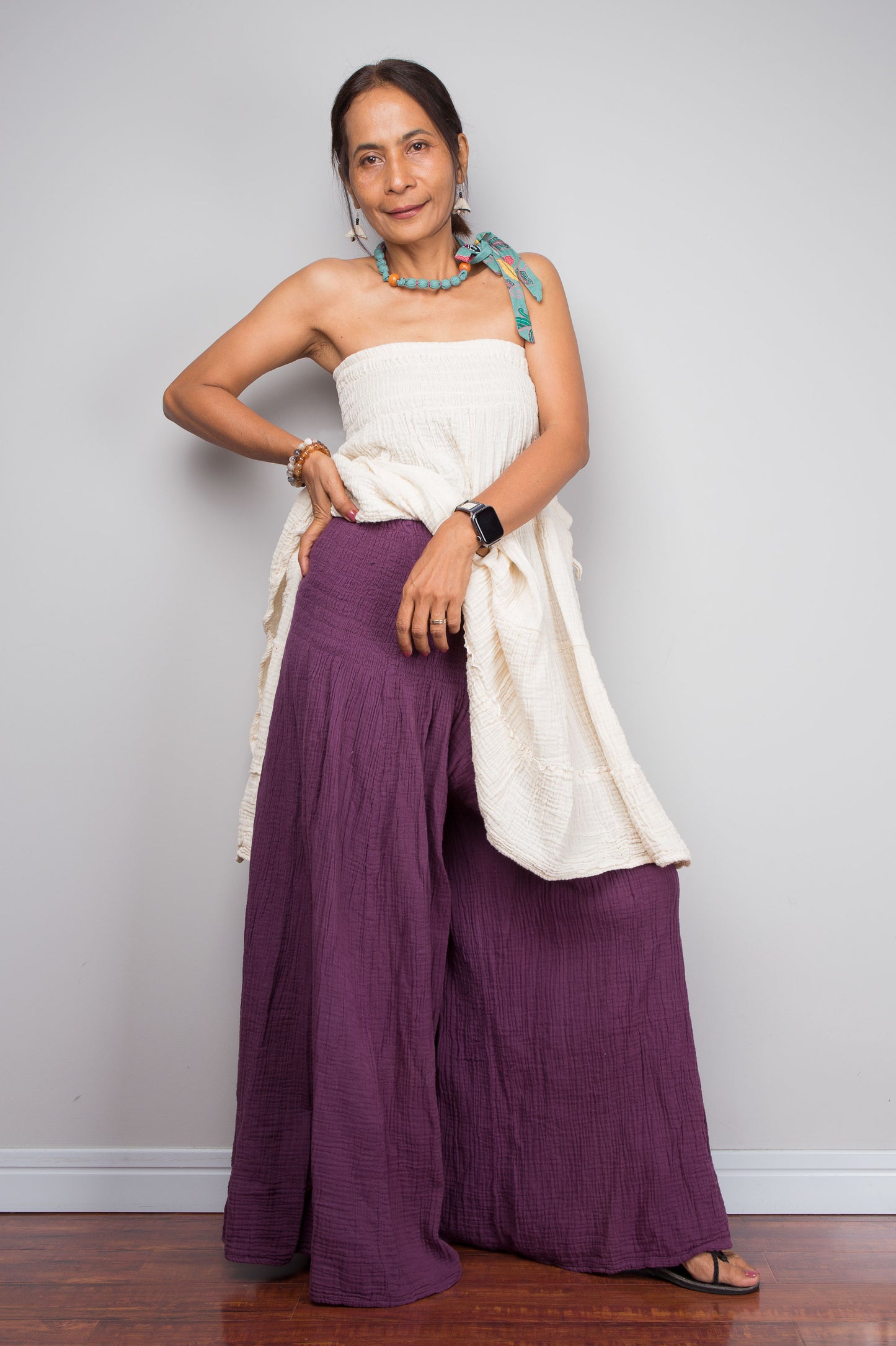 Woman wearing a white top and purple wide leg cotton pants against a plain background