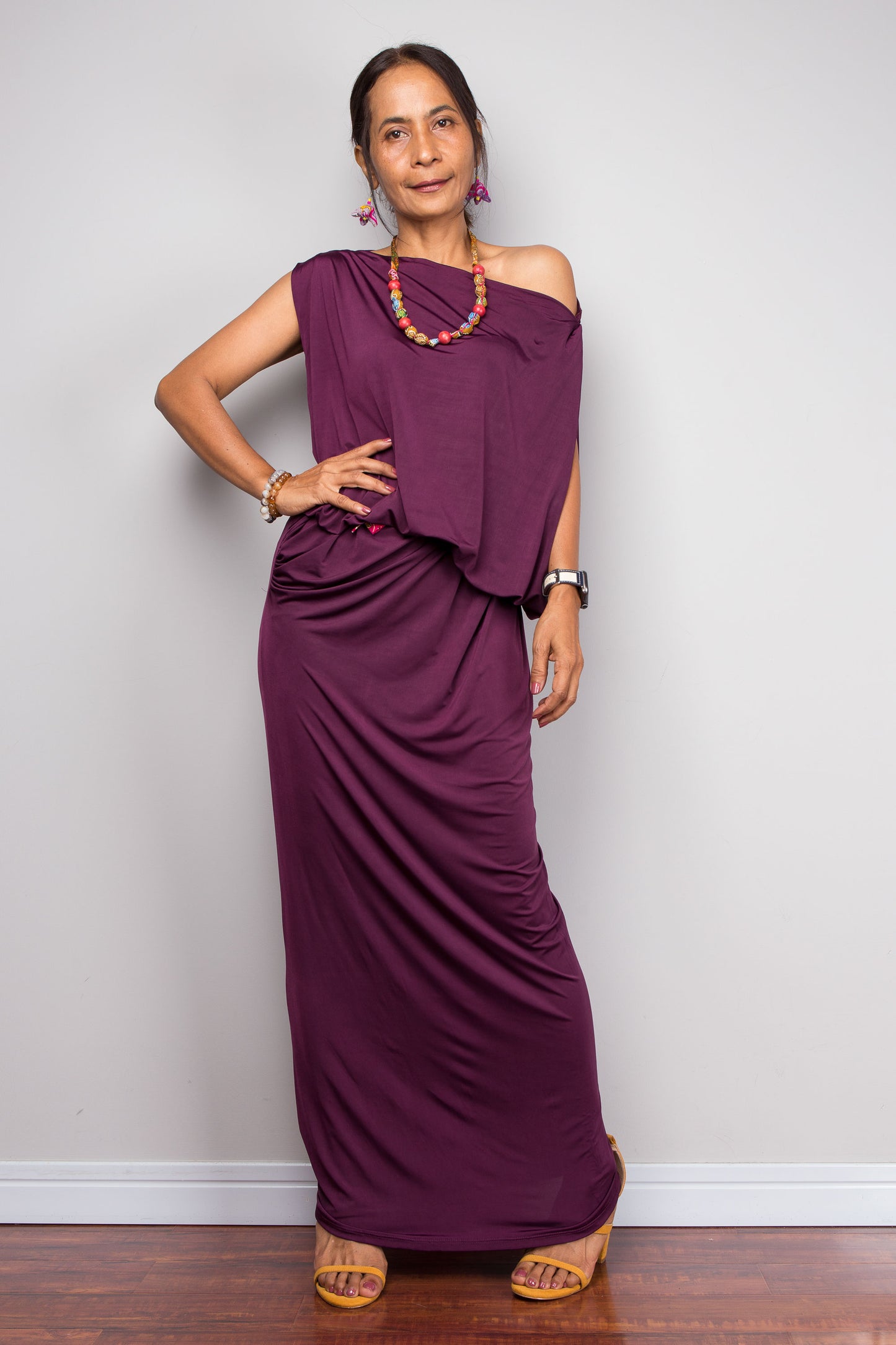 Woman wearing a sophisticated plum purple evening maxi dress featuring an asymmetric one-shoulder design and beautiful draped fabric

