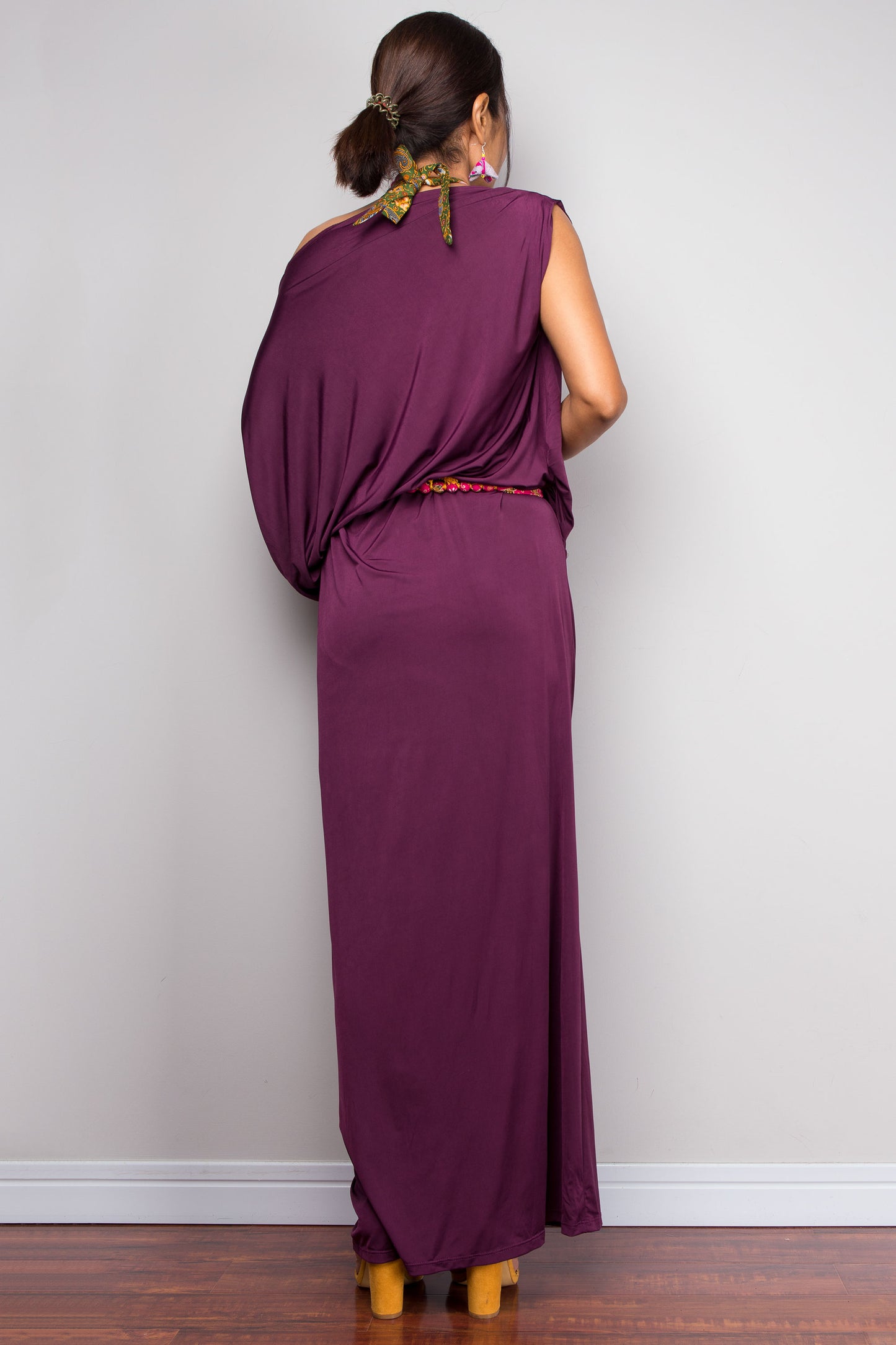 Woman wearing a long purple dress against a plain wall.