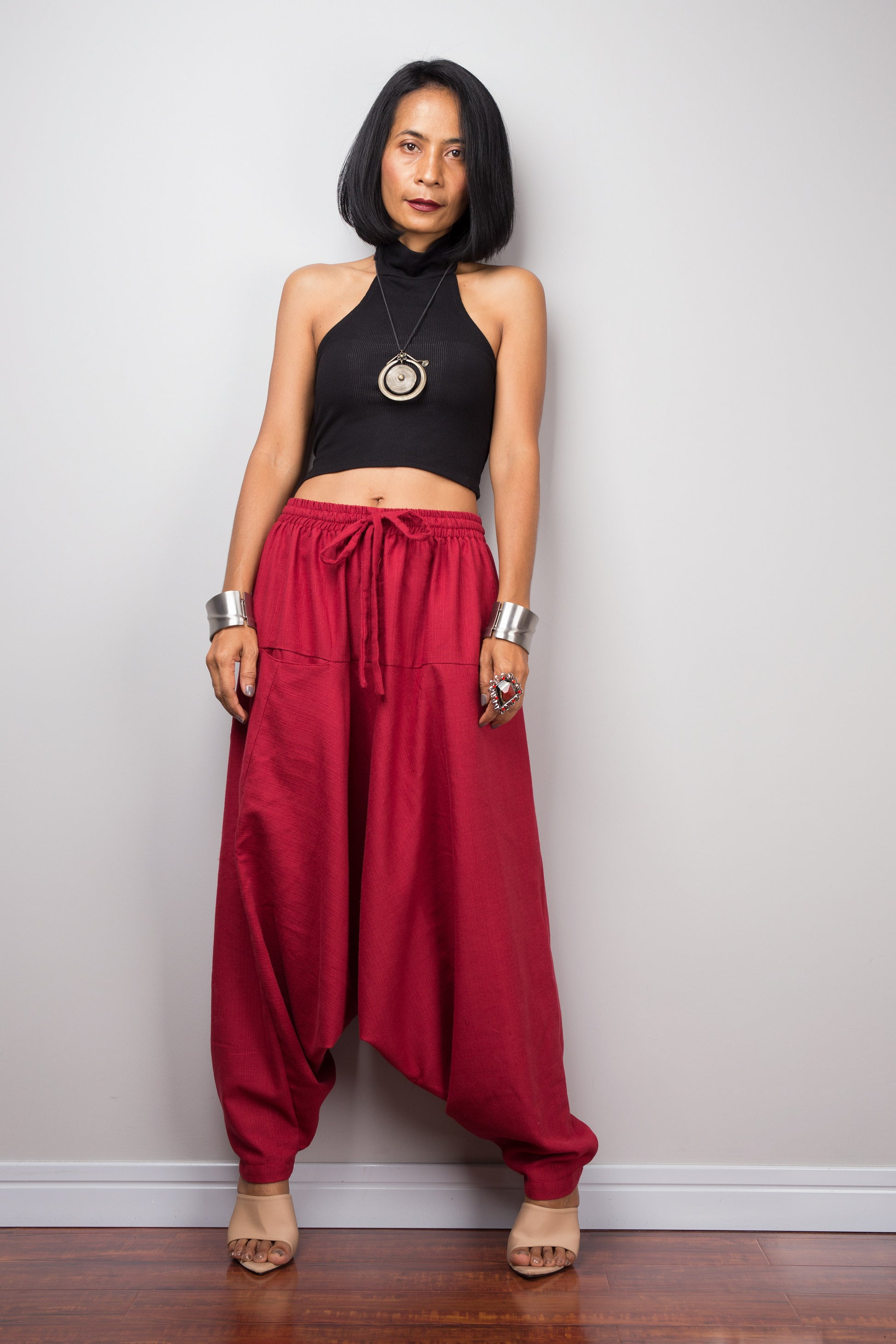 Model wearing red harem pants with a loose fit and black top, standing against a plain background, showcasing the full-length view.