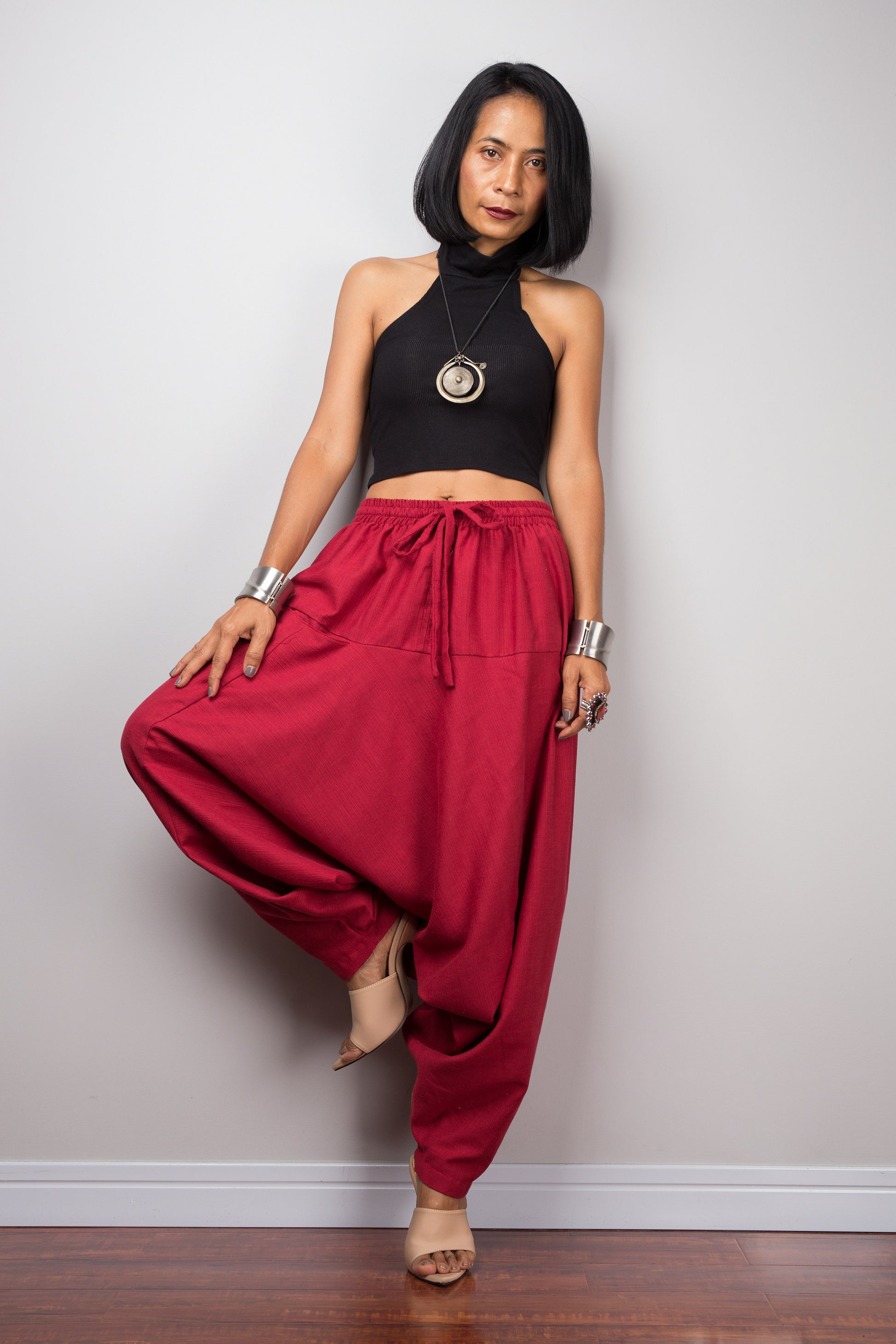 Model wearing red harem pants with a loose fit, standing lotus pose against a plain background, showcasing the full-length view.