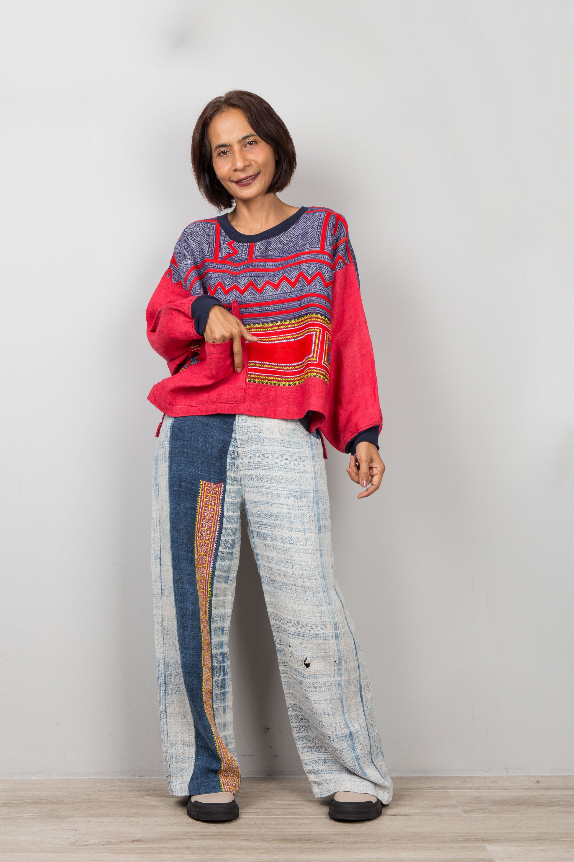 Woman wearing a patchwork hemp sweater with indigo batik and patterned pants against a plain background