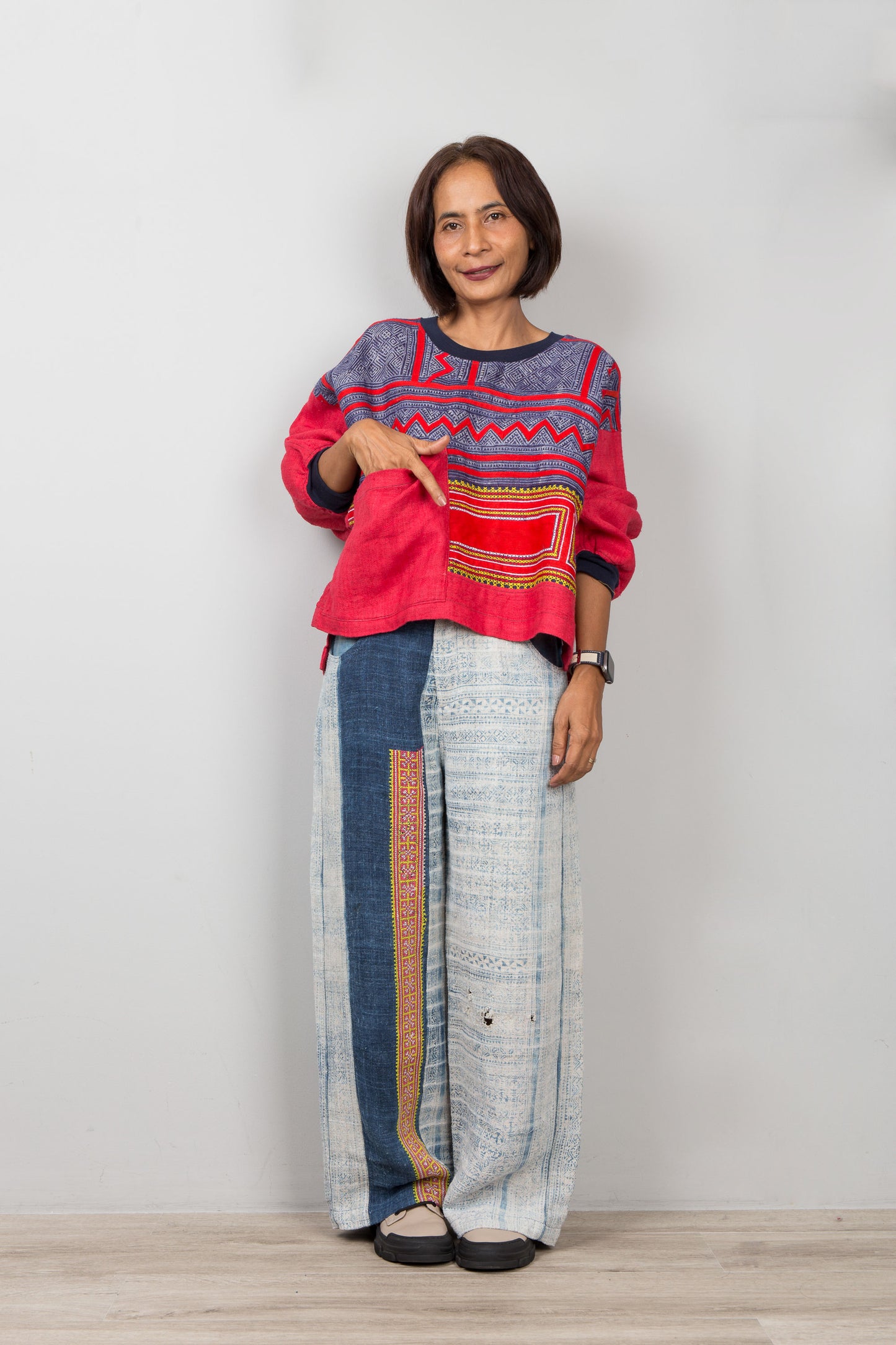 Woman wearing a colorful red sweatshirt and patterned pants on a plain background