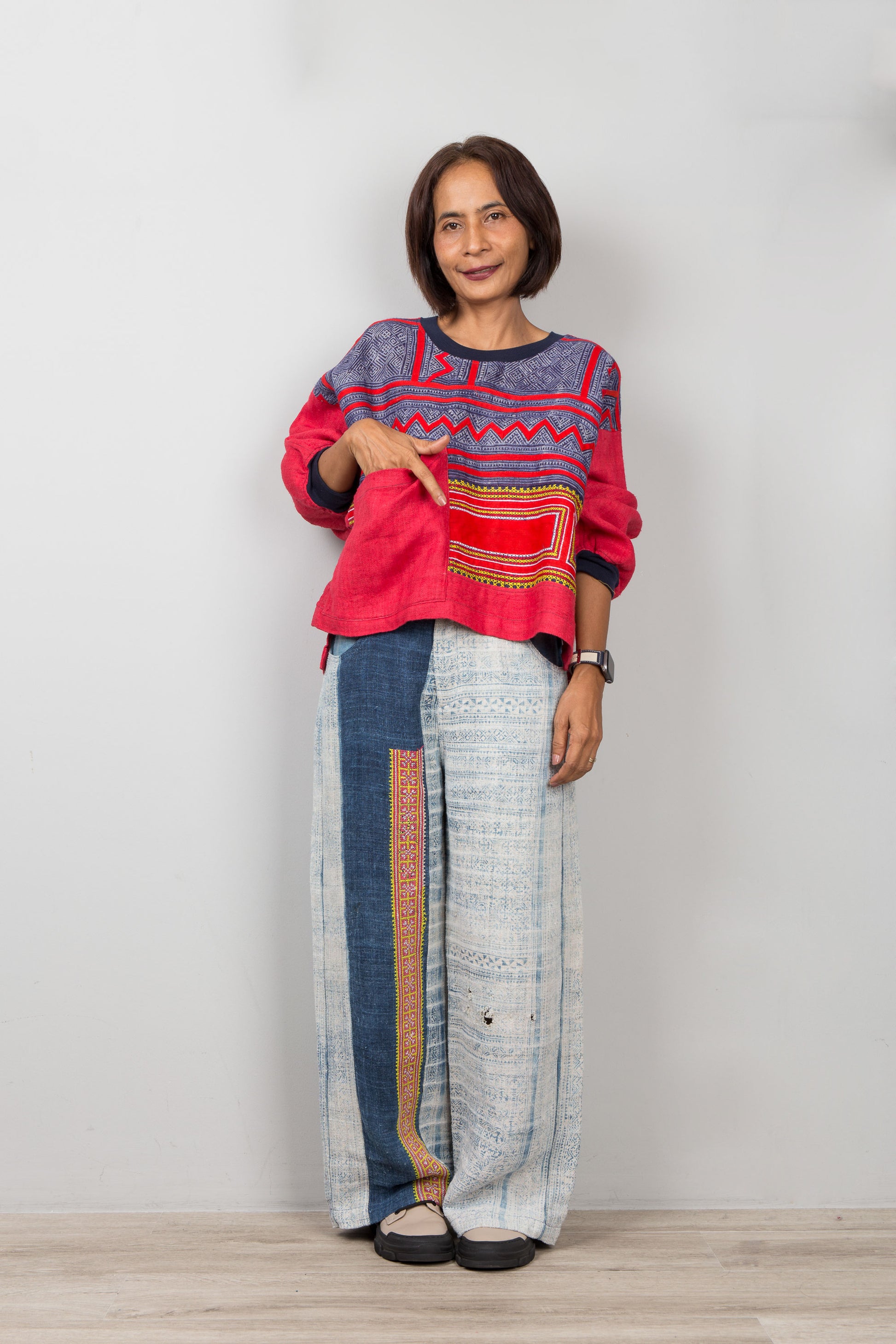 Woman wearing a colorful red sweatshirt and patterned pants on a plain background