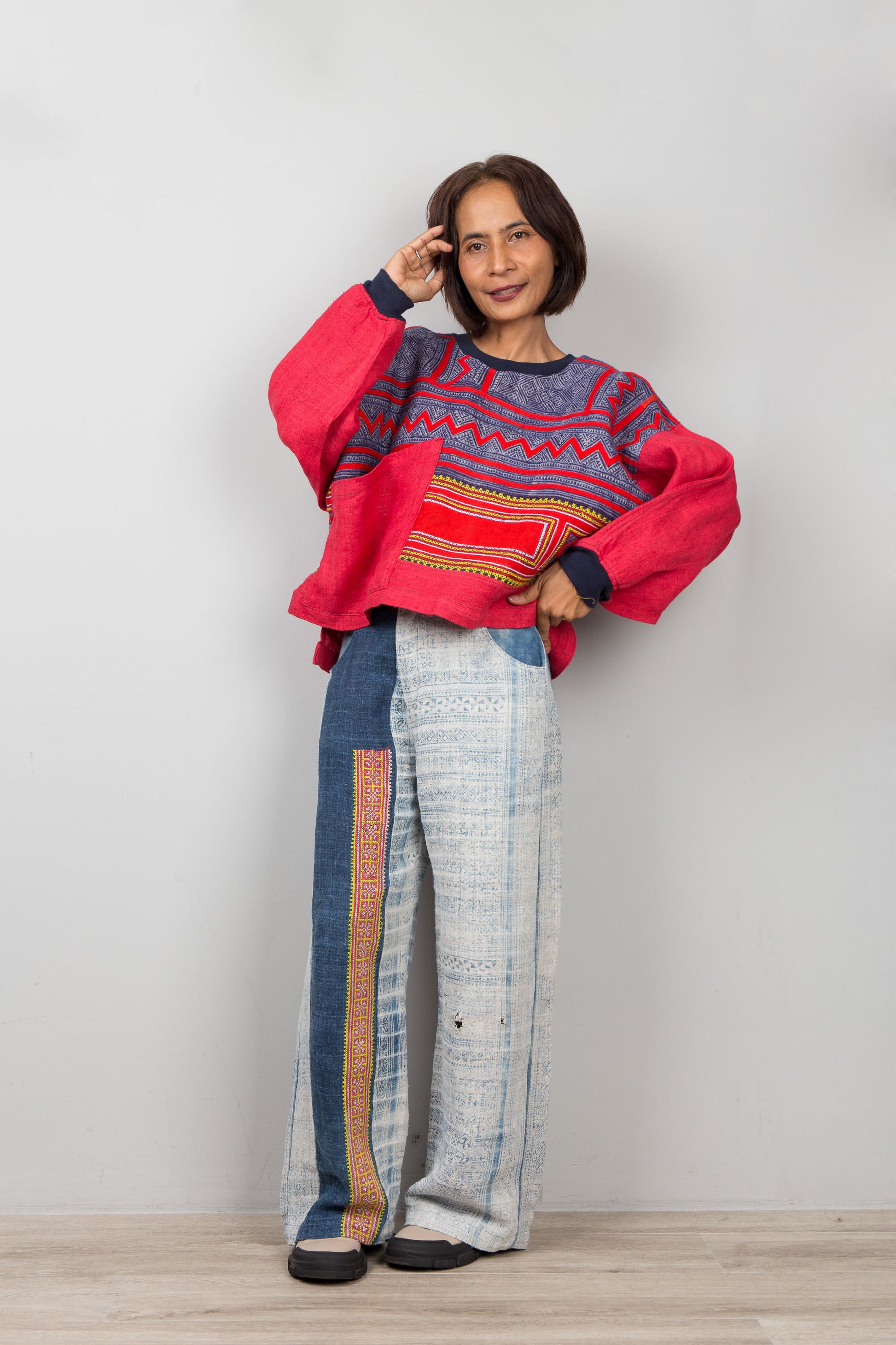 Person wearing a colorful patchwork 
sweater and patterned pants against a plain background