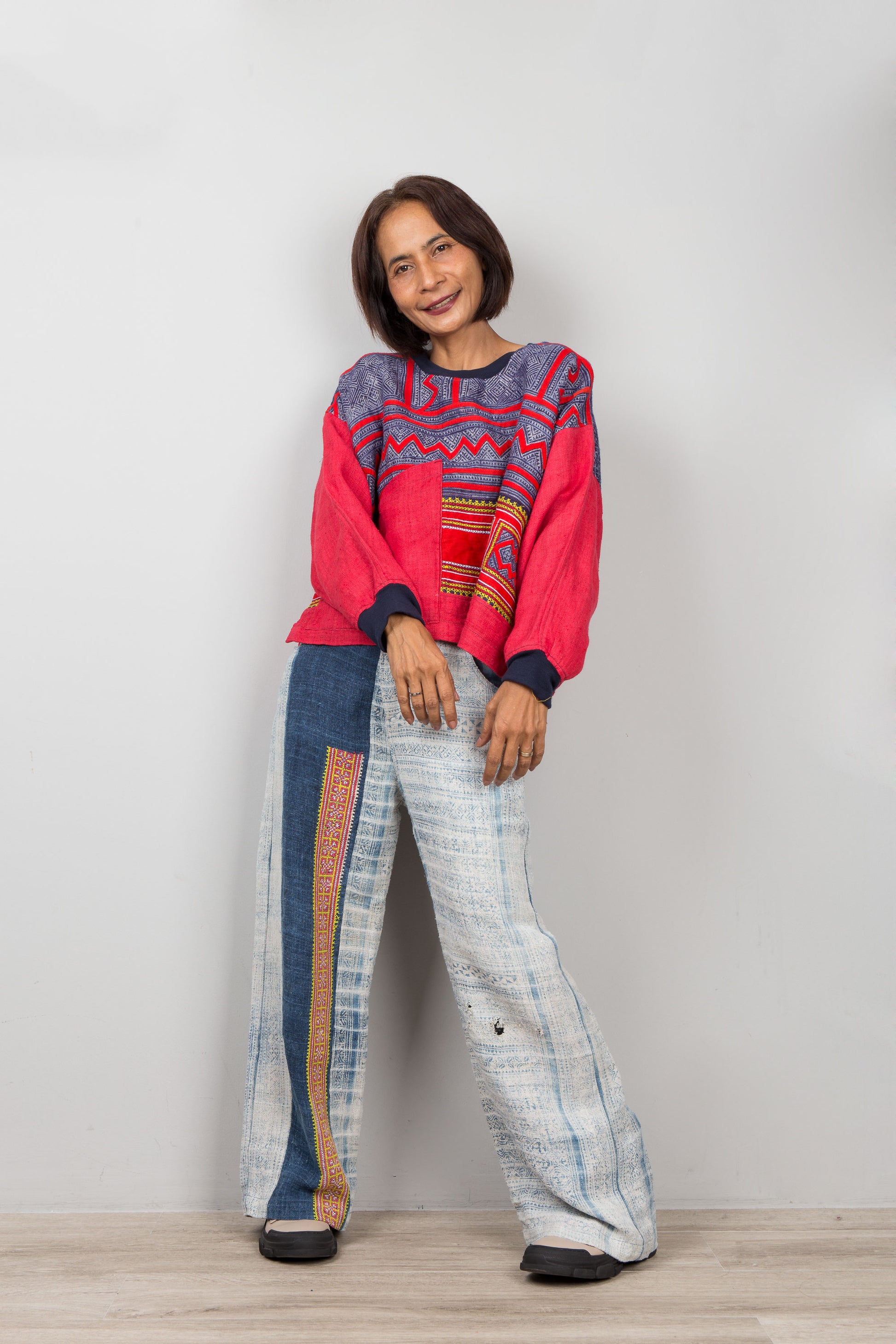 Person wearing a colorful red sweater and patterned pants on a plain background