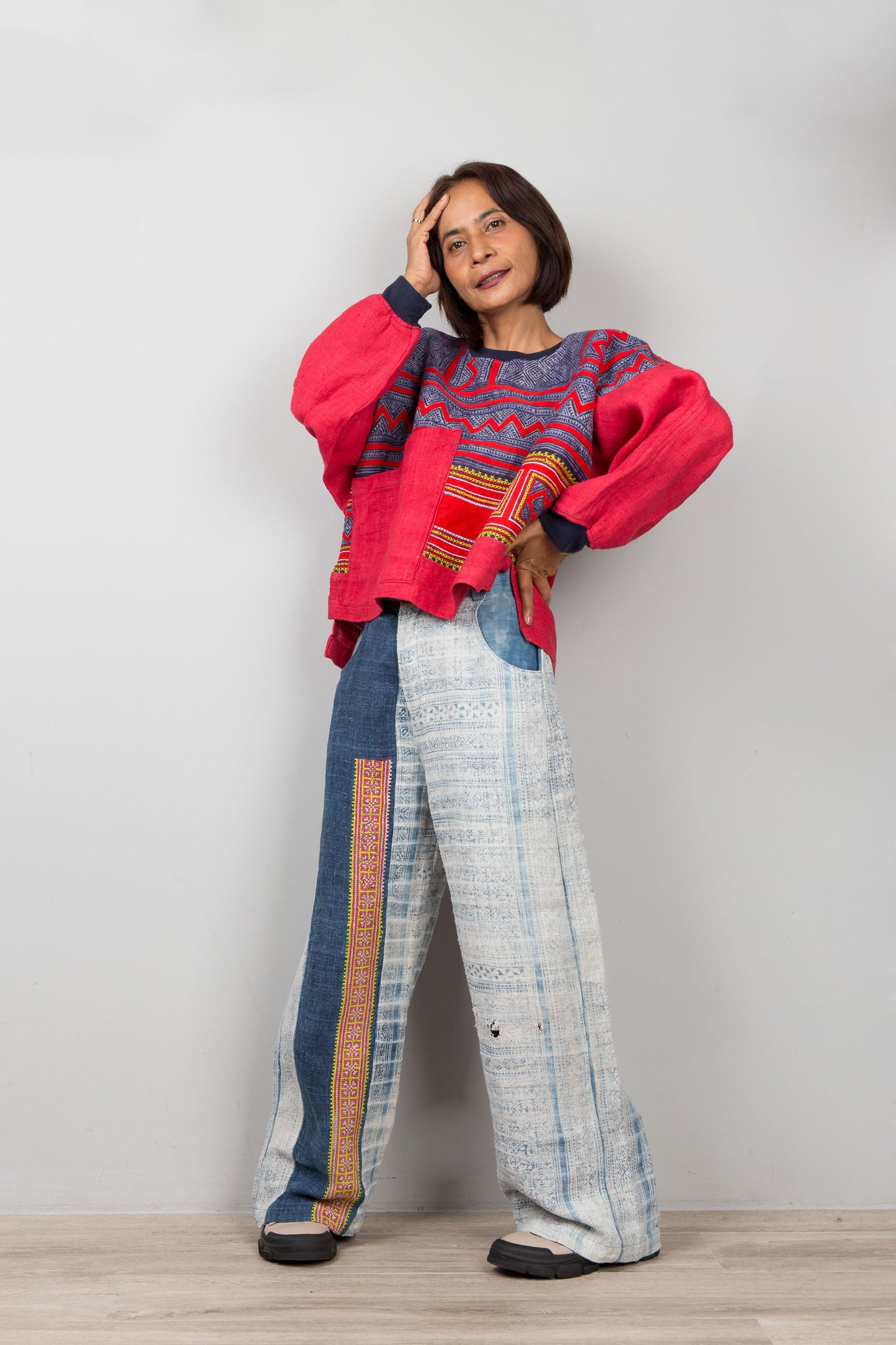 Woman wearing a colorful red sweater and patterned pants against a plain background