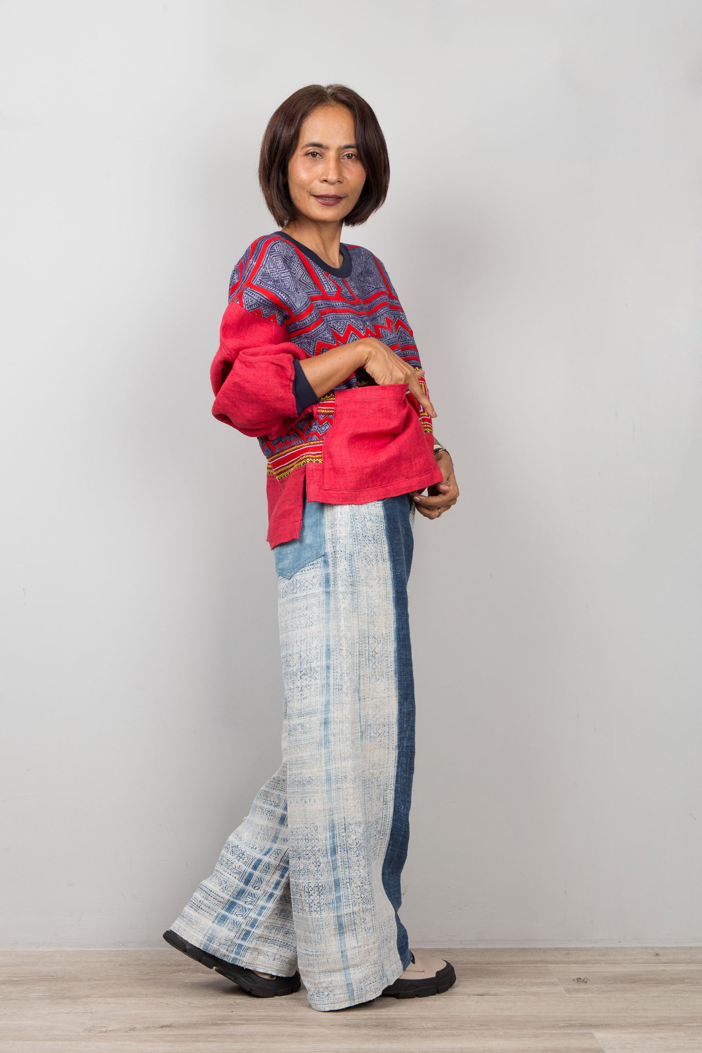 Woman wearing a red and blue patterned sweater top with light blue plaid pants on a white background
