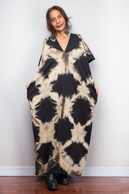 Woman wearing an original Nuichan brand, reverse tie dye kaftan dress against a white wall.