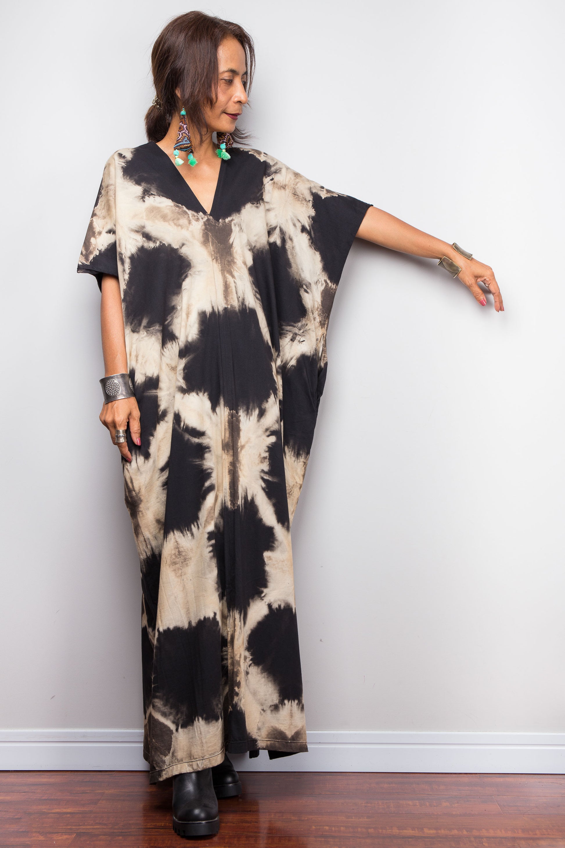 Woman wearing an original Nuichan brand, reverse tie dye kaftan dress in black and sand colour against a white wall.
