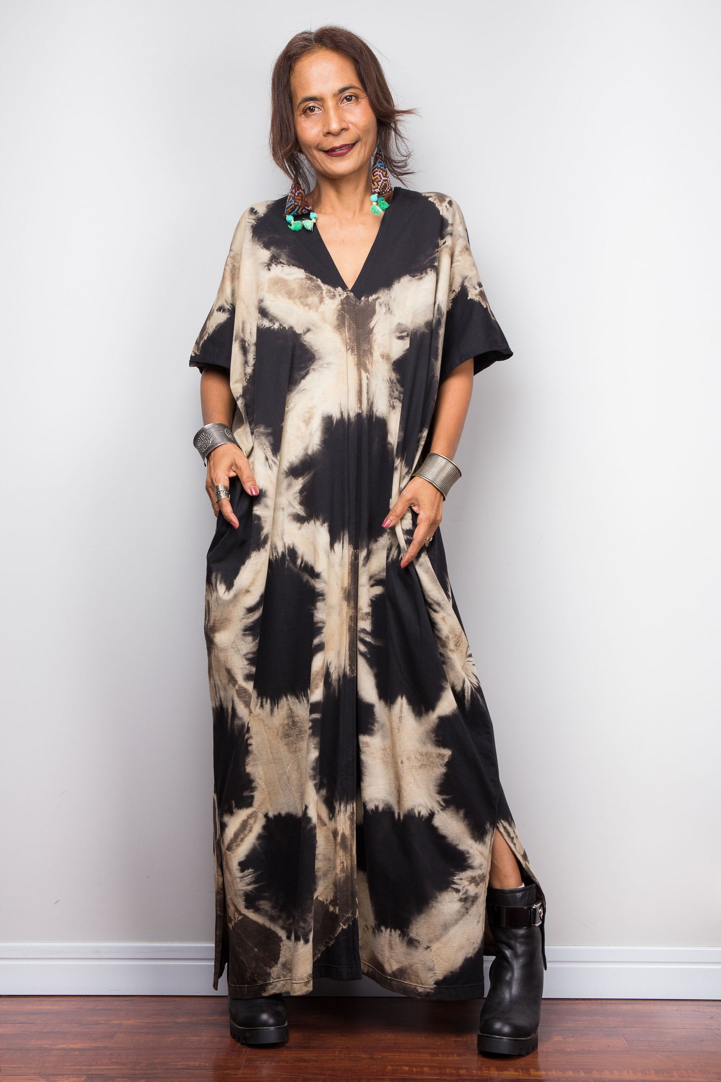 Petite Woman wearing an original Nuichan brand, reverse tie dye kaftan dress in black and sand tones against a white wall.