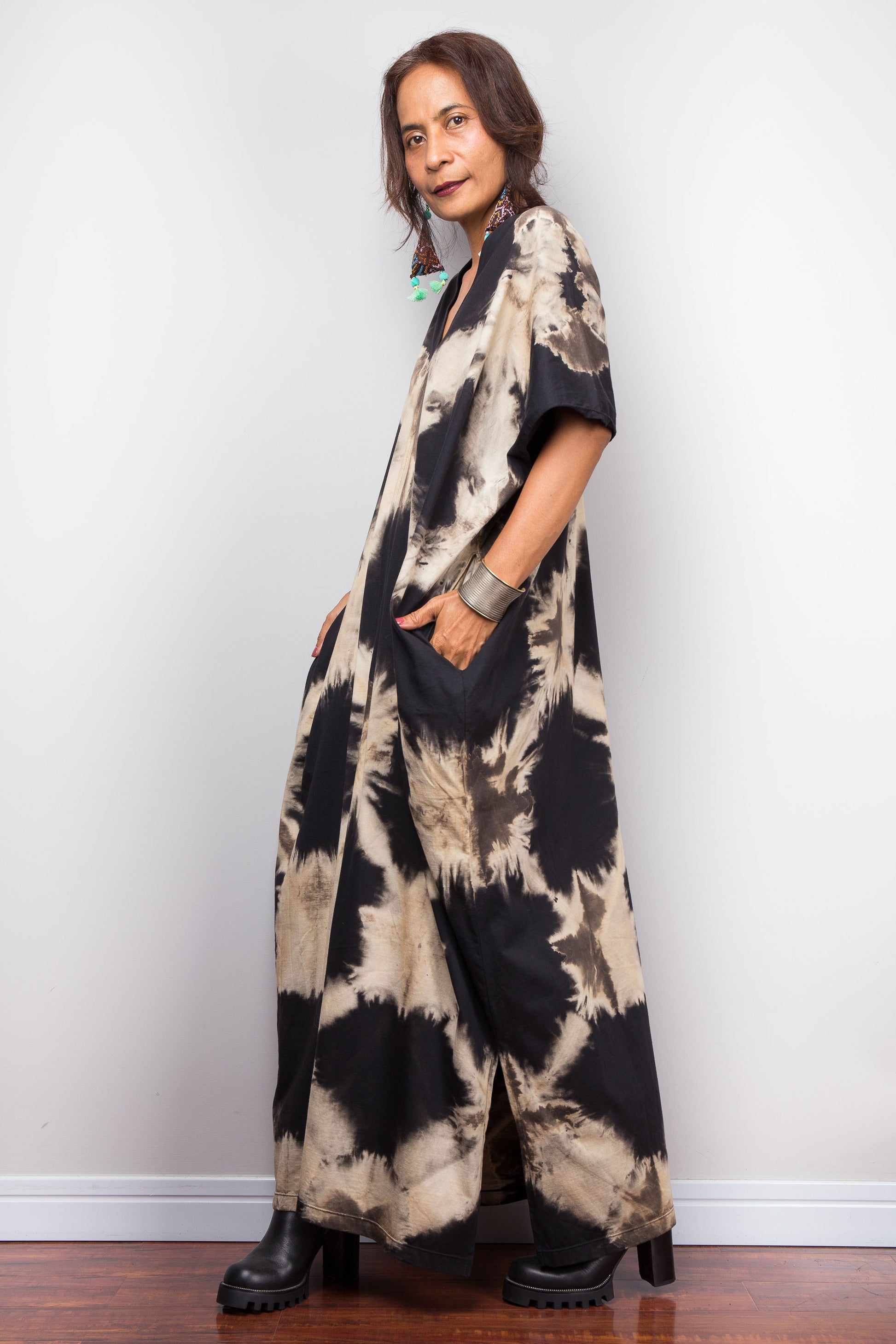 Woman wearing an original Nuichan brand, reverse tie dye kaftan dress, with pockets, against a white wall.