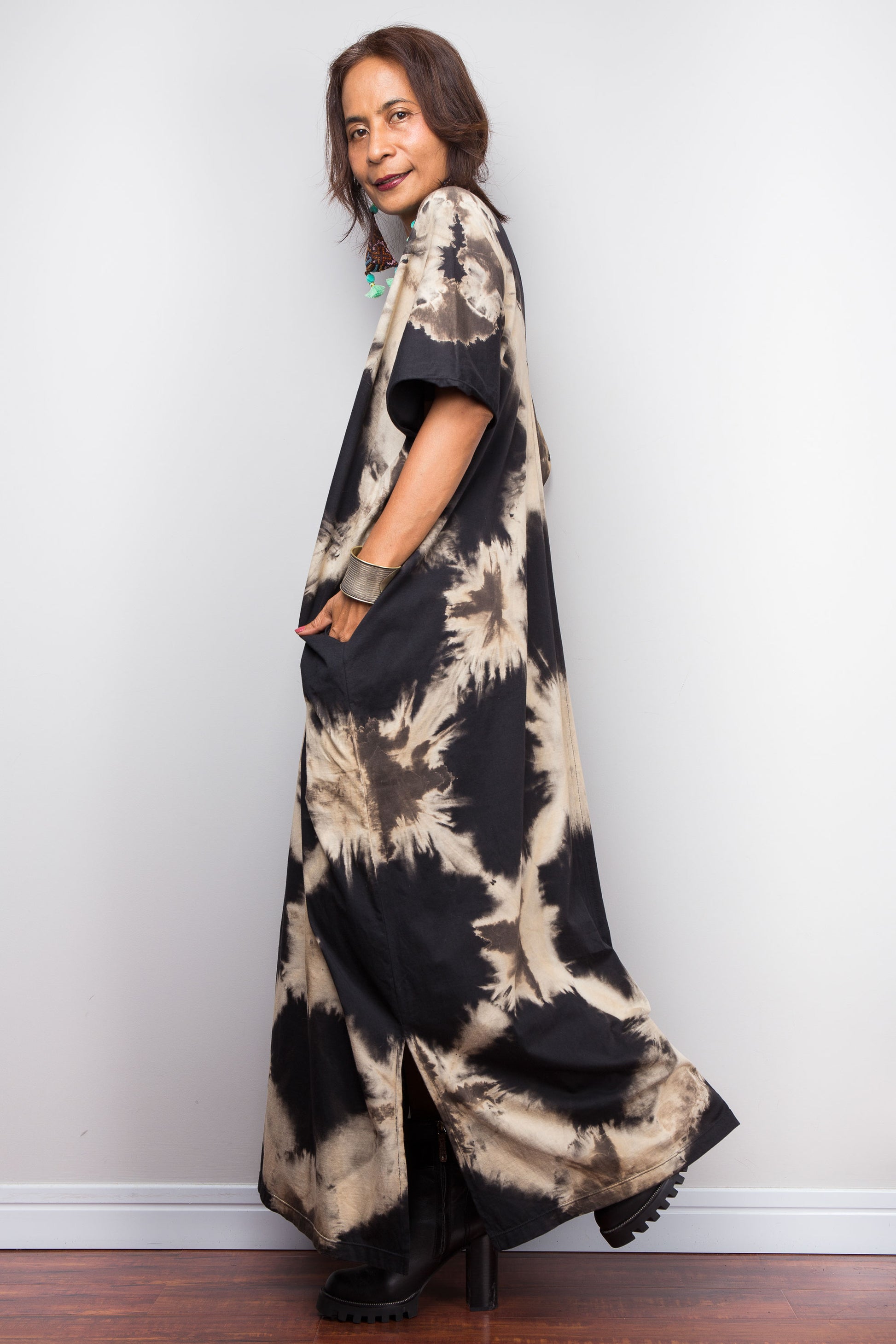 Woman wearing an original Nuichan brand, reverse tie dye kaftan dress, with pockets, against a grey wall.