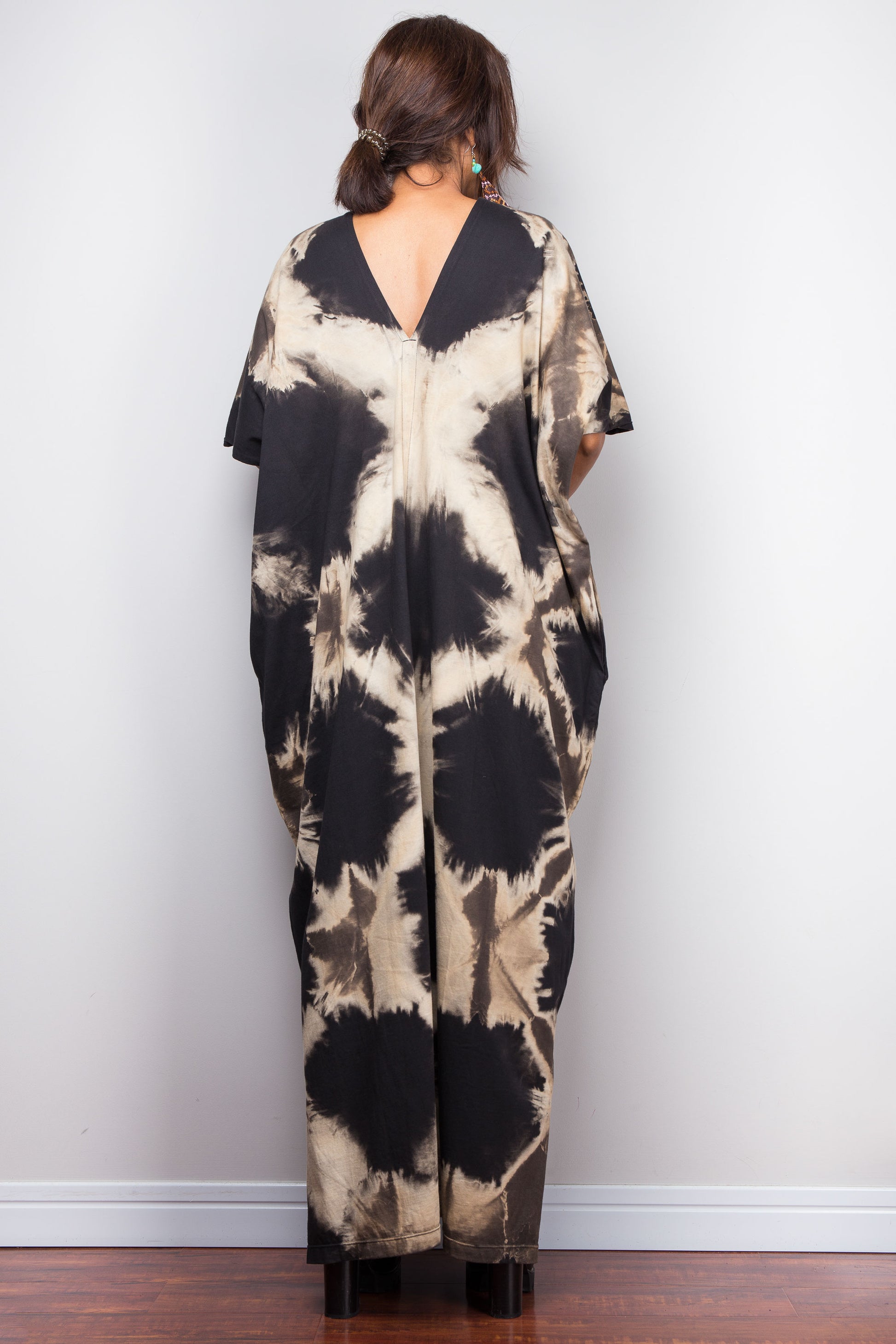 Petite woman wearing an original Nuichan brand reverse tie-dye dress with a V-neck and open back against a white wall.