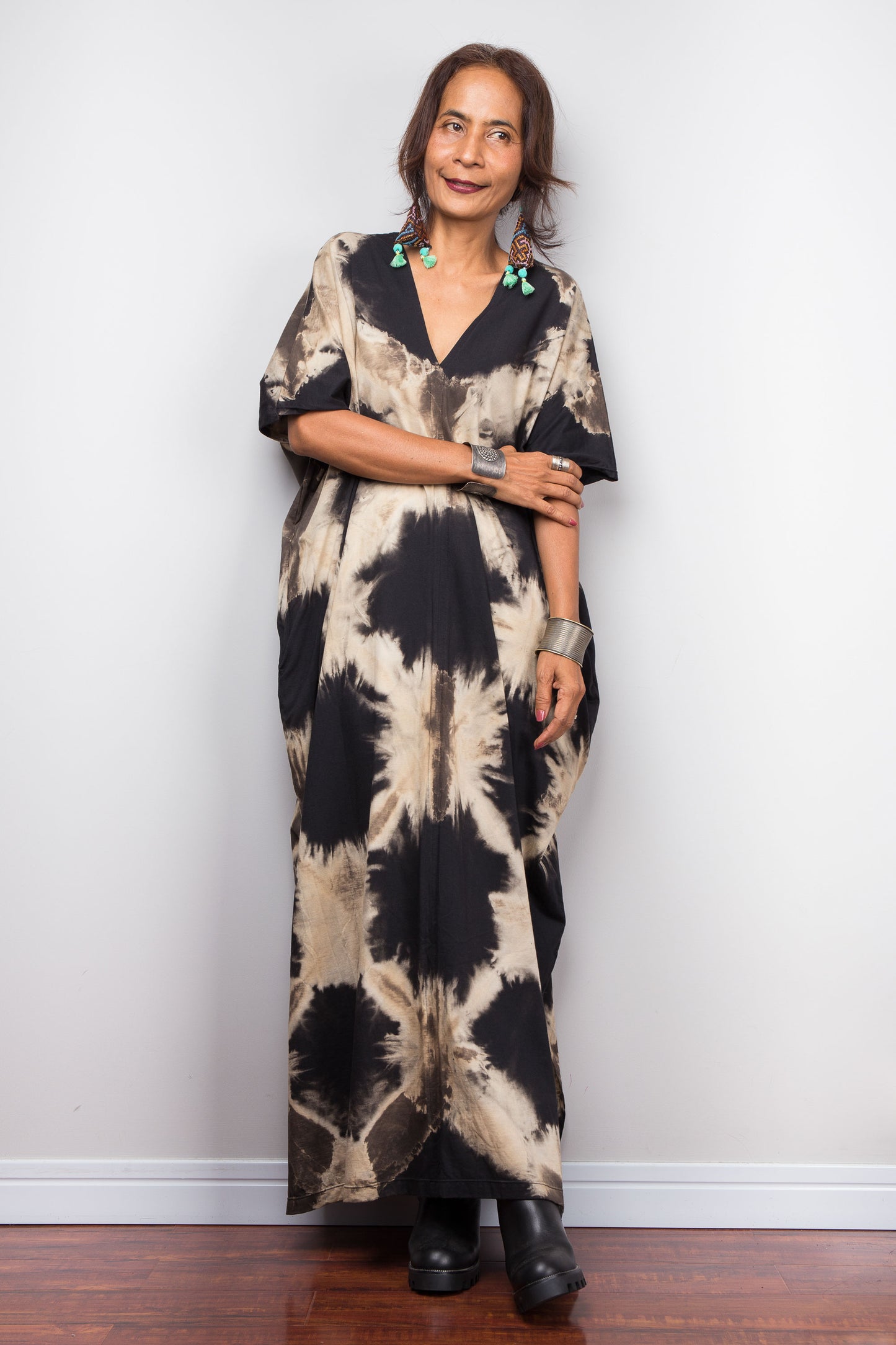 Woman wearing a tie-dye dress standing against a white wall.