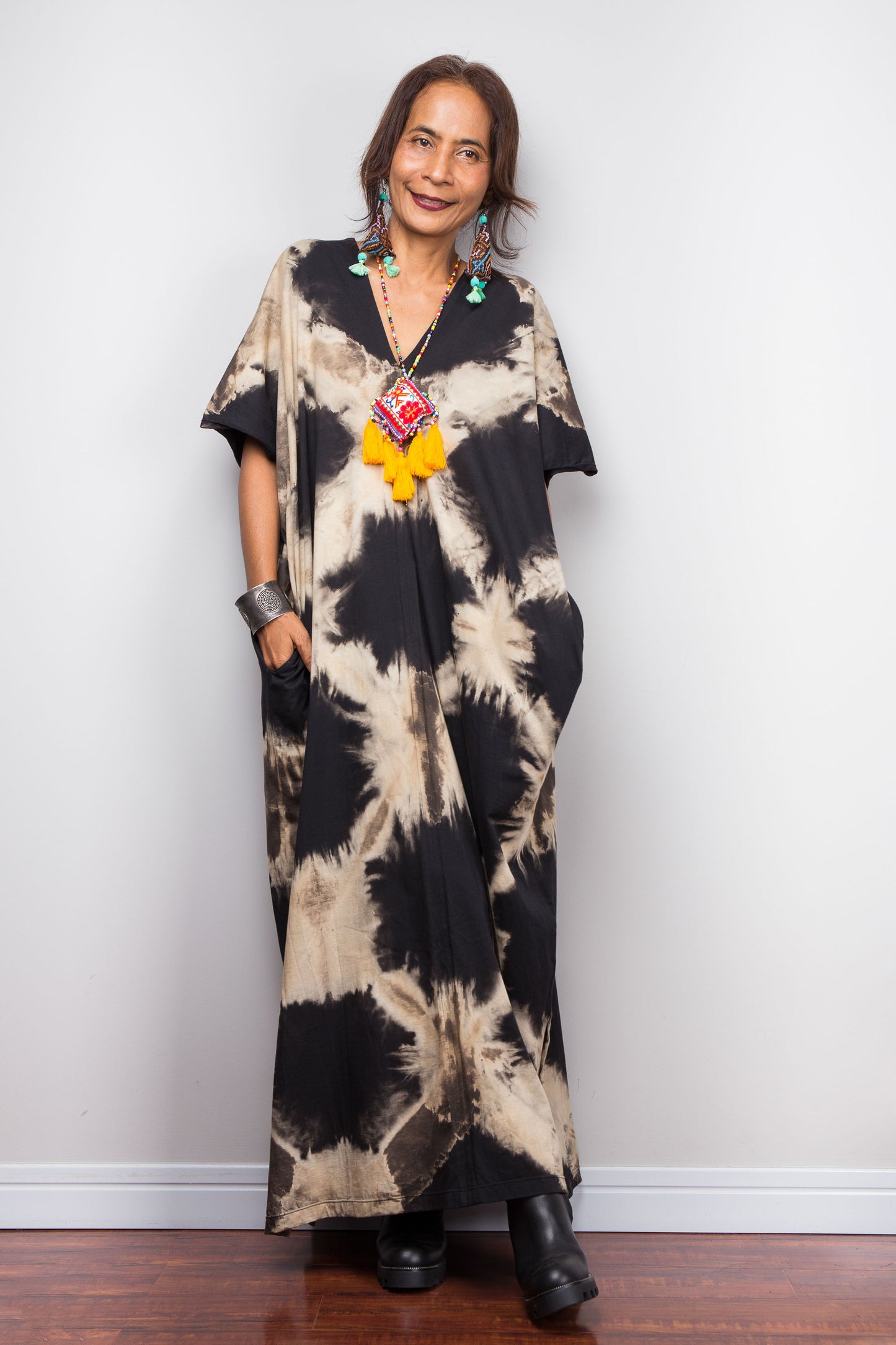 Petite woman wearing an original Nuichan brand, reverse tie dye kaftan dress against a white wall.