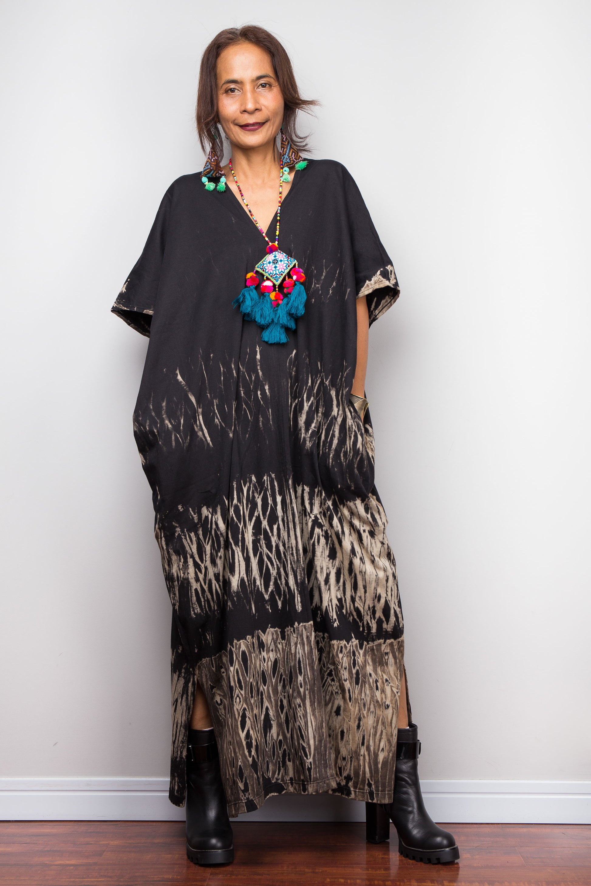 Woman wearing a reverse tie dye dress with a colorful necklace against a white wall.