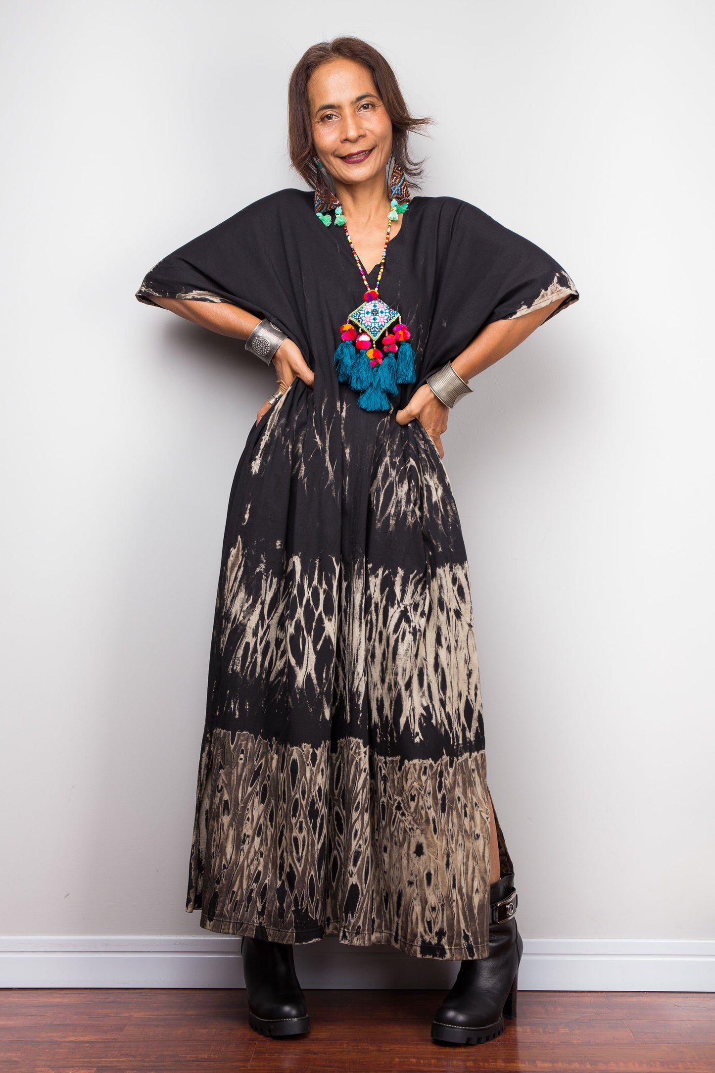 Woman wearing a black and patterned dress with a colorful necklace against a white wall. Reverse tie dye dress by Nuichan