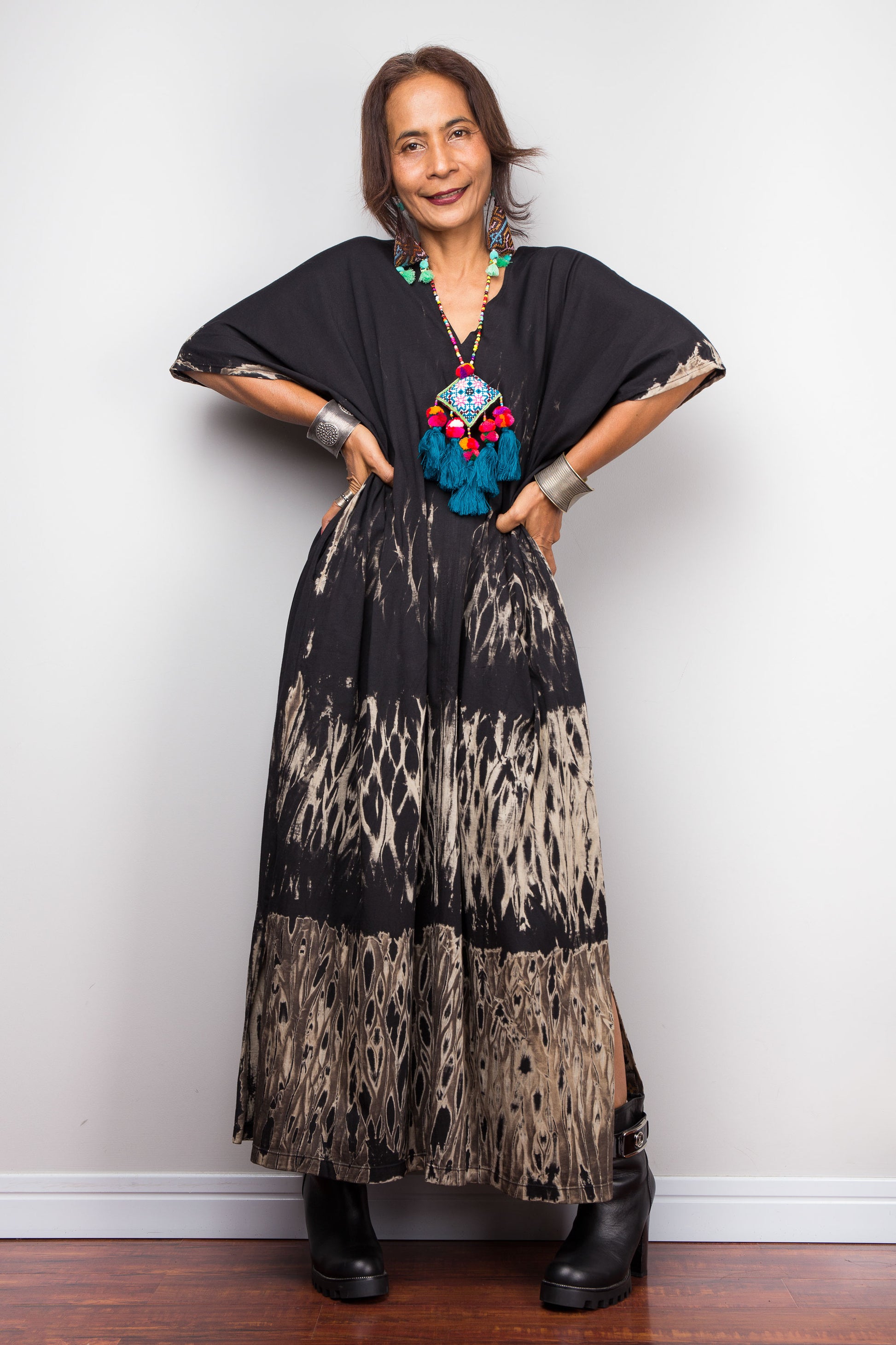 Woman wearing a black and patterned dress with a colorful necklace against a white wall. Reverse tie dye dress by Nuichan