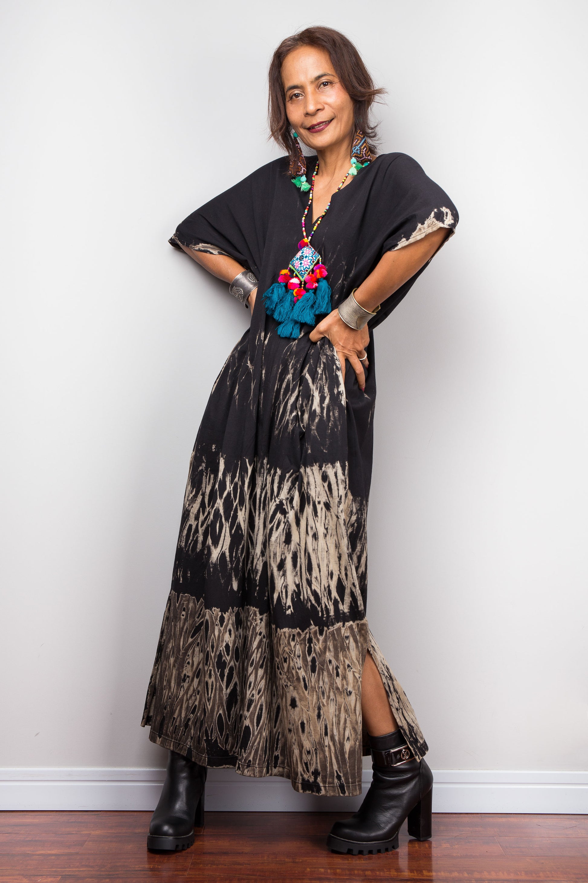 Woman wearing a black and patterned reverse tie dye dress with a colorful necklace against a white wall.