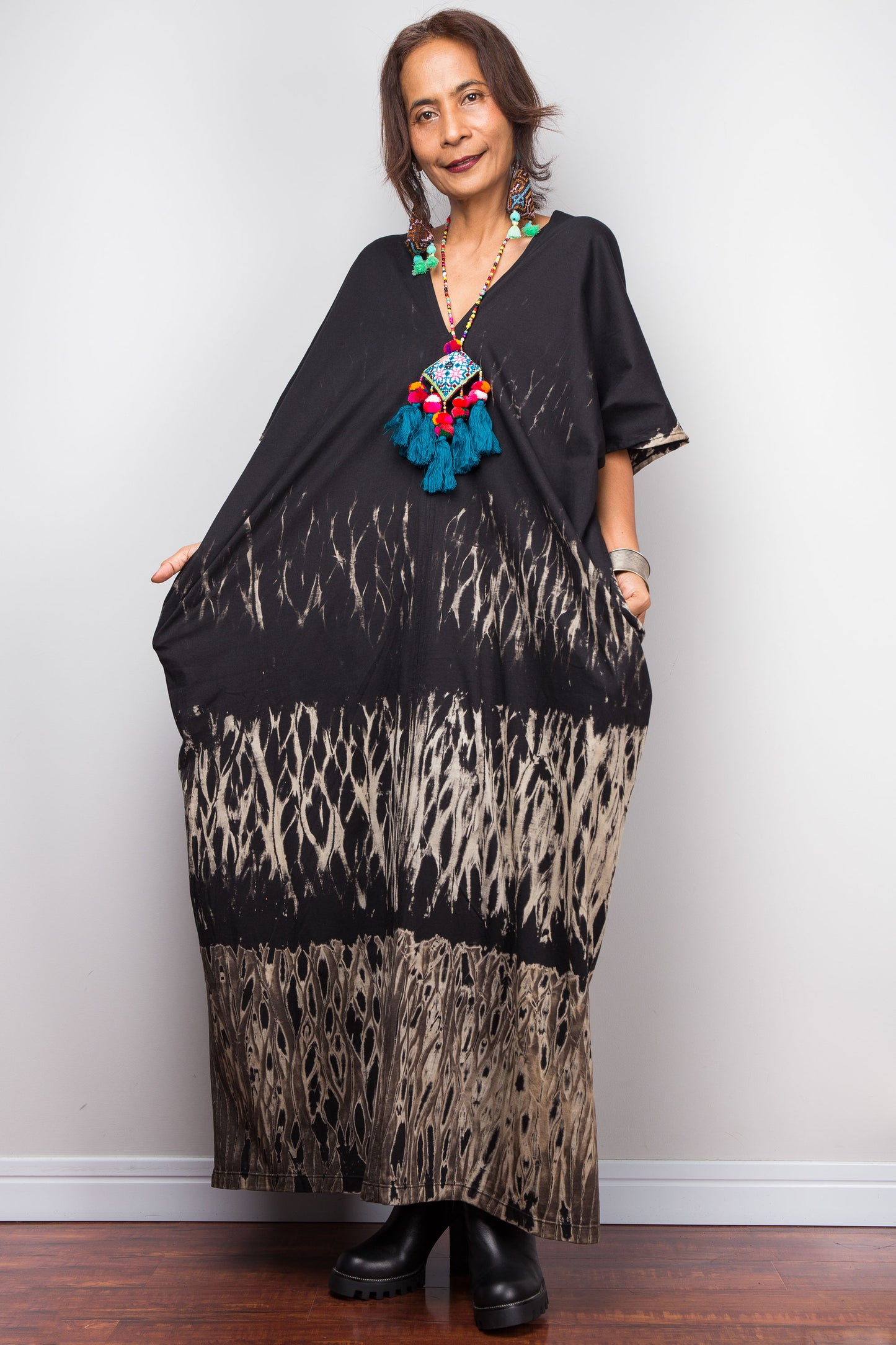 Woman wearing a reverse tie dye dress with a colorful boho necklace against a white wall.