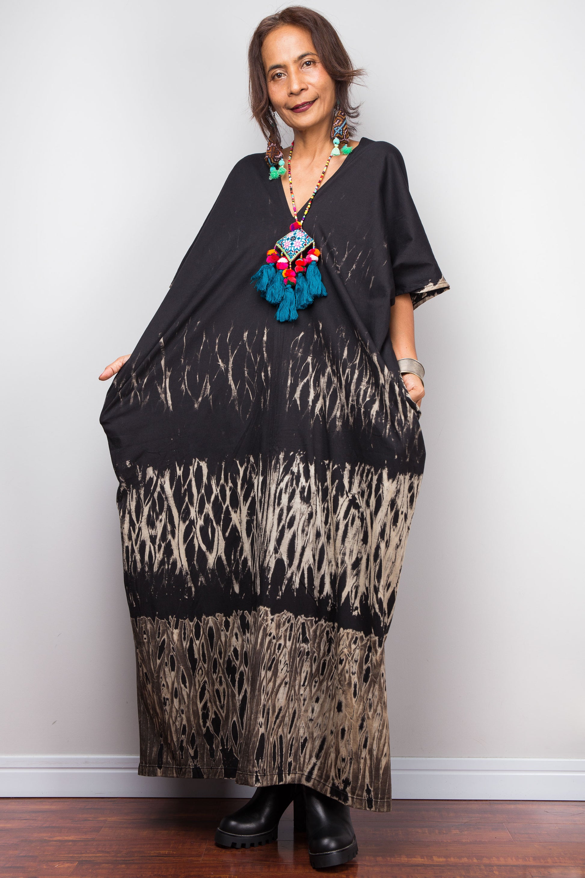 Woman wearing a reverse tie dye dress with a colorful boho necklace against a white wall.
