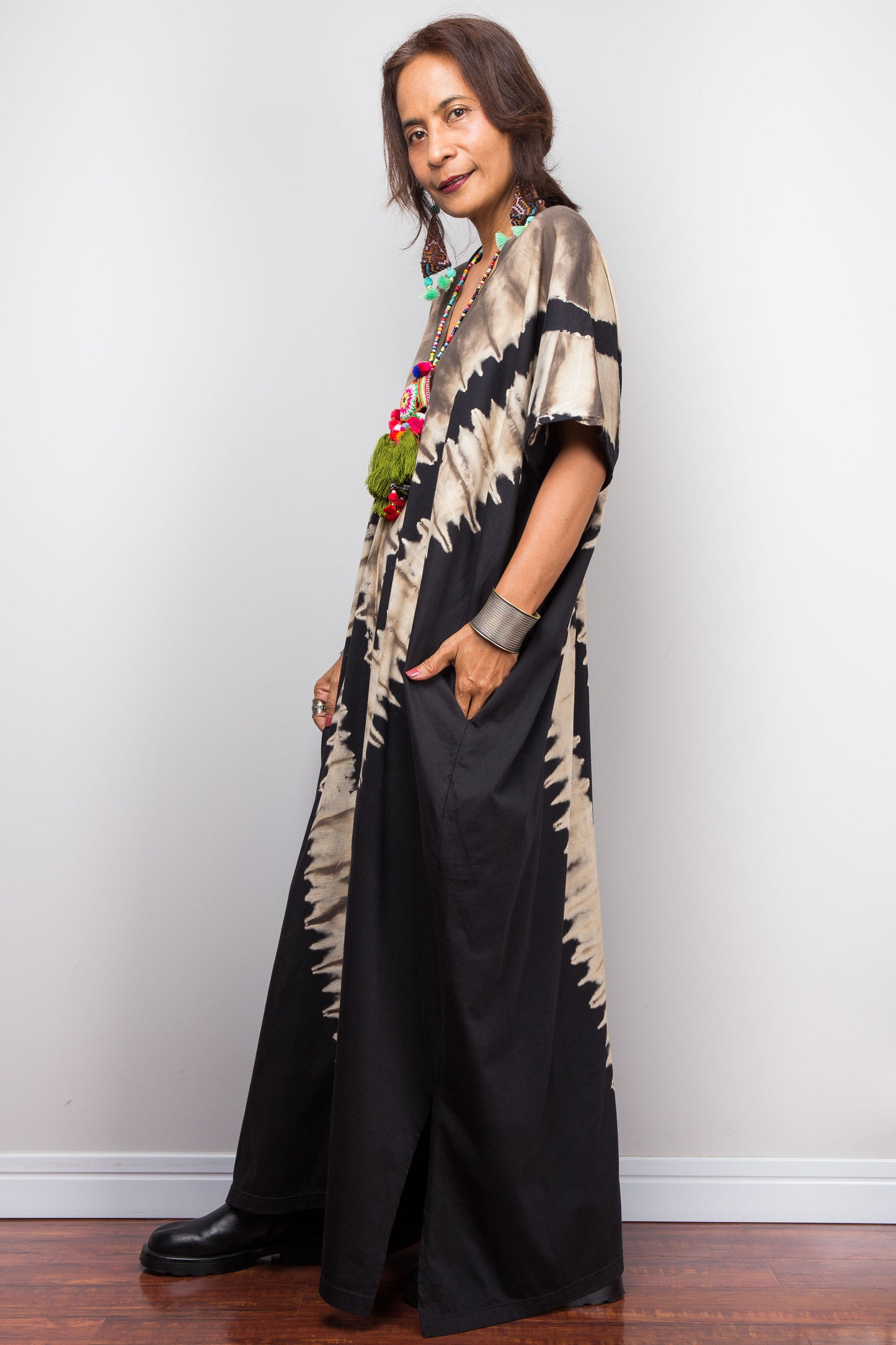 Authentic Nuichan brand oversized black and sand reverse tie dye kaftan dress, a cotton boho maxi dress with short sleeves and pockets worn by a petite model, facing sideways.