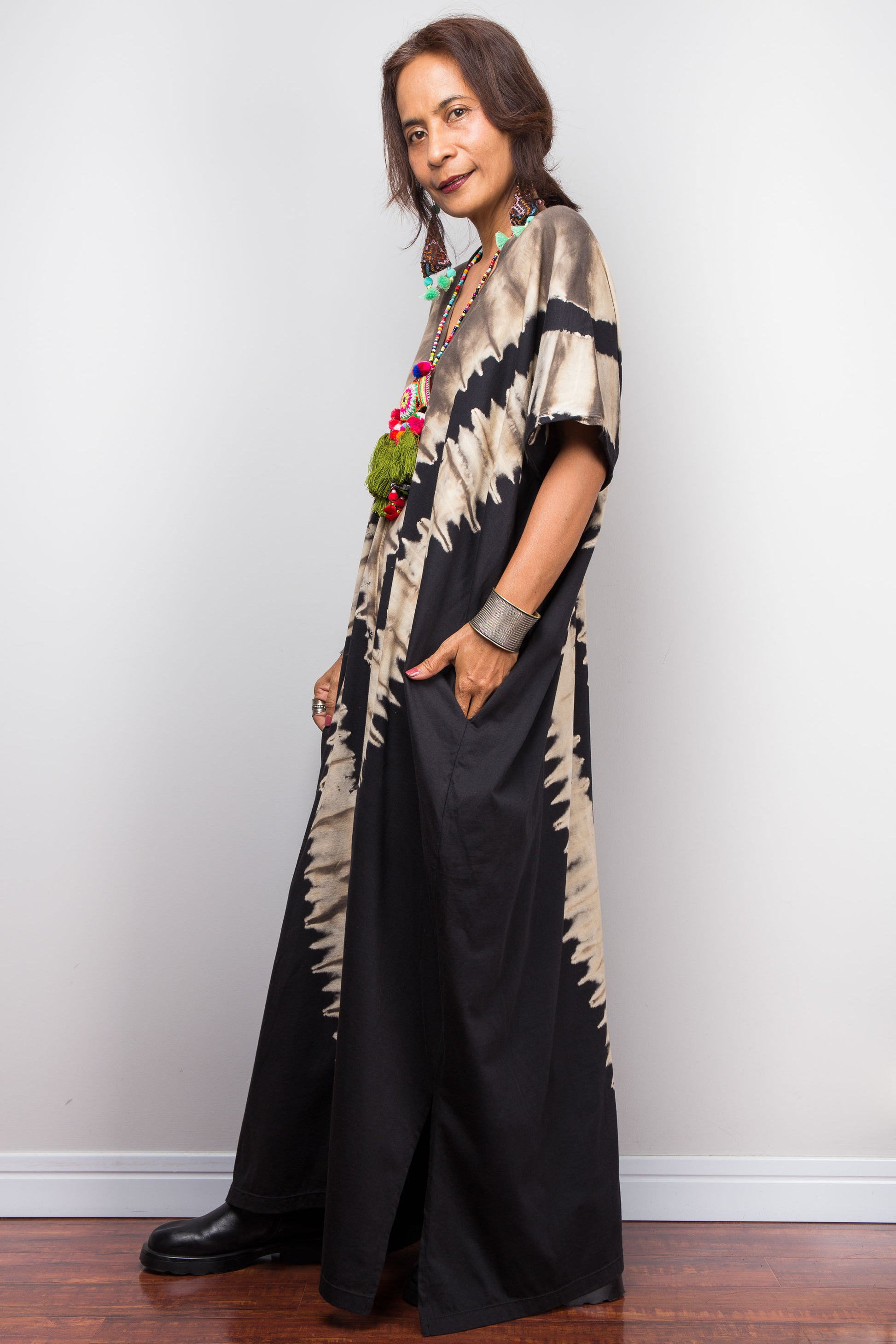 Authentic Nuichan brand oversized black and sand reverse tie dye kaftan dress, a cotton boho maxi dress with short sleeves and pockets worn by a petite model, facing sideways.
