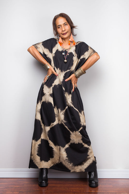 Woman wearing a long, reverse tie dye kaftan dress against a plain background