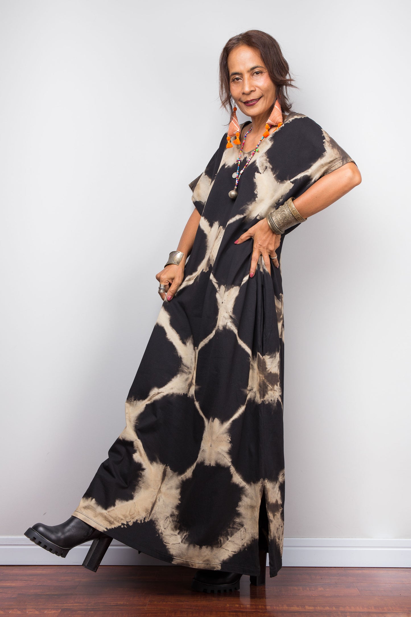 Woman wearing a black and beige patterned reverse tie dye dress against a white wall.