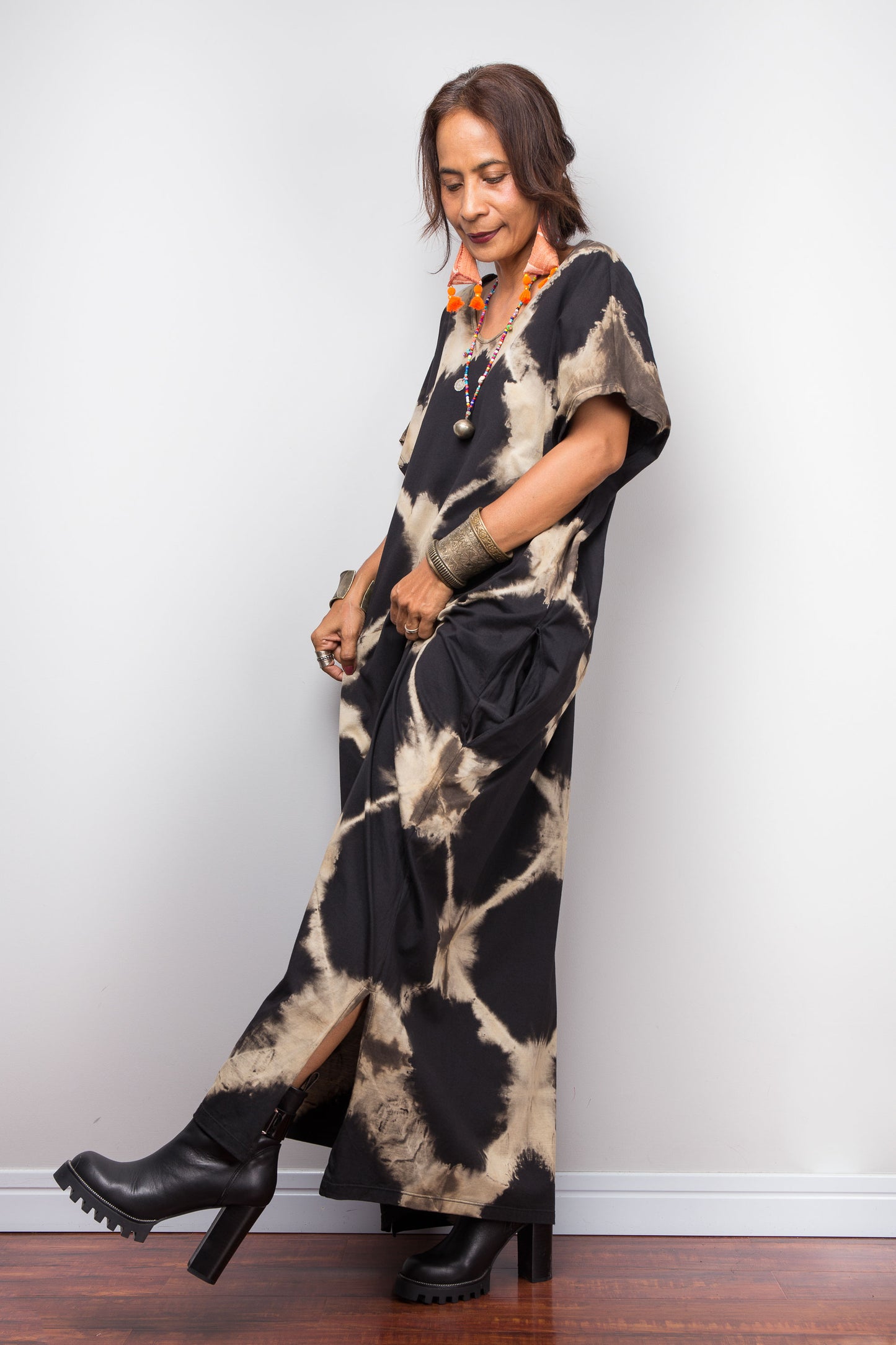 Woman wearing a tie-dye dress with black and beige pattern against a white wall.